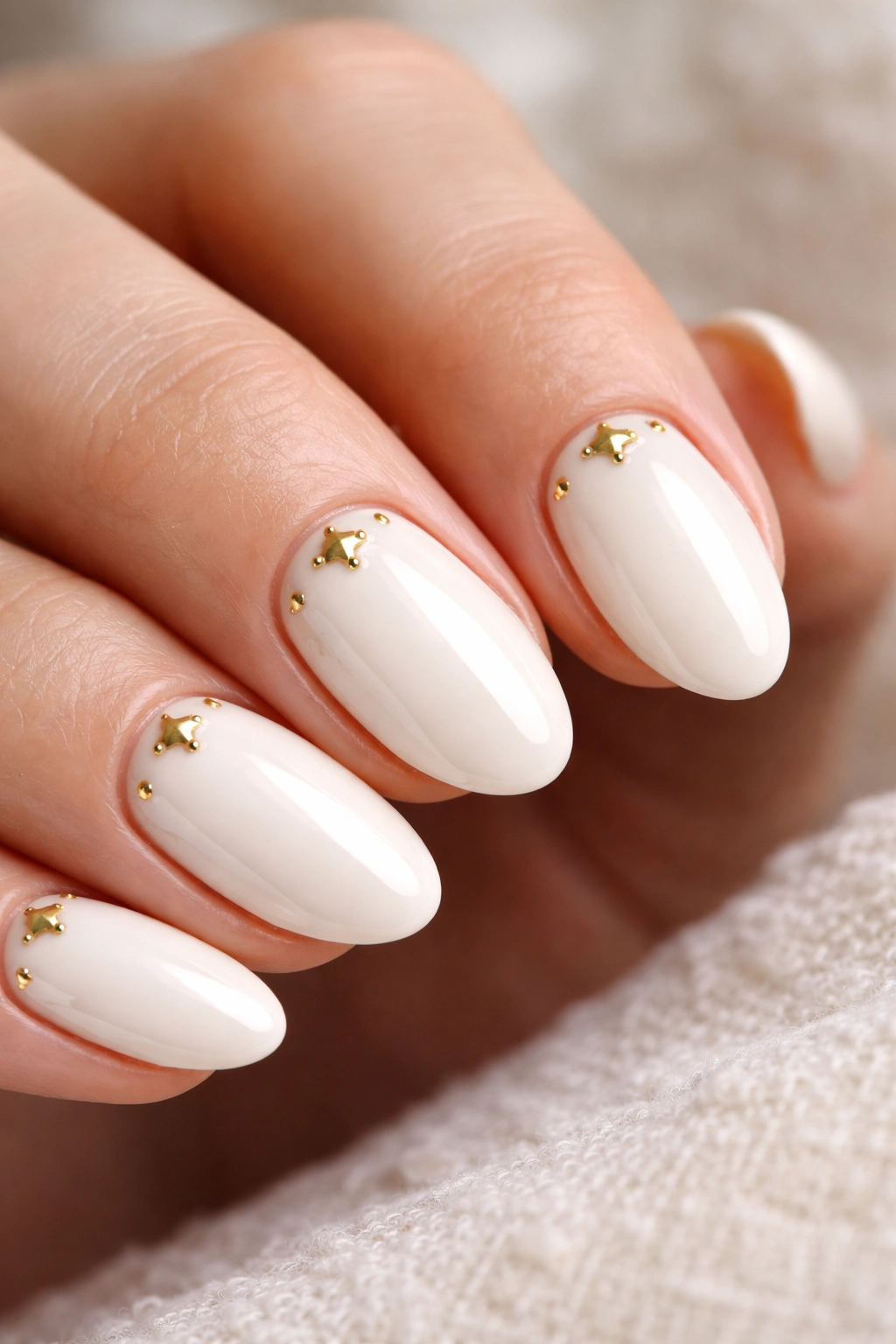 Close-up of ivory almond nails with gold stars near the cuticle