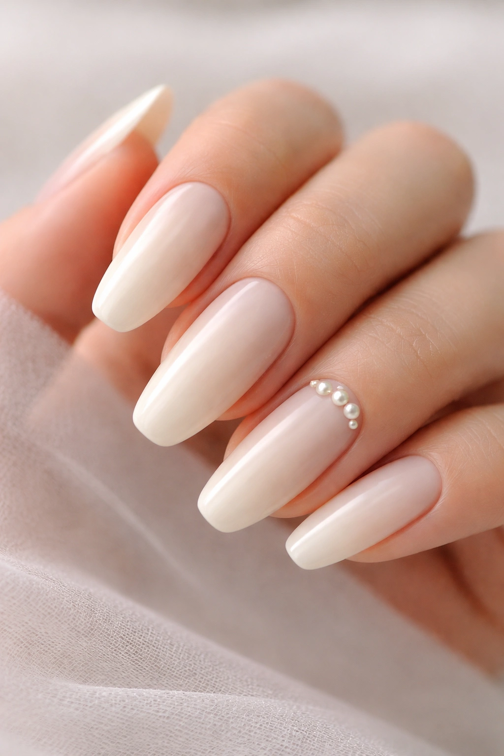 Close-up of soft ivory ballerina nails with tiny pearl accents near the cuticle