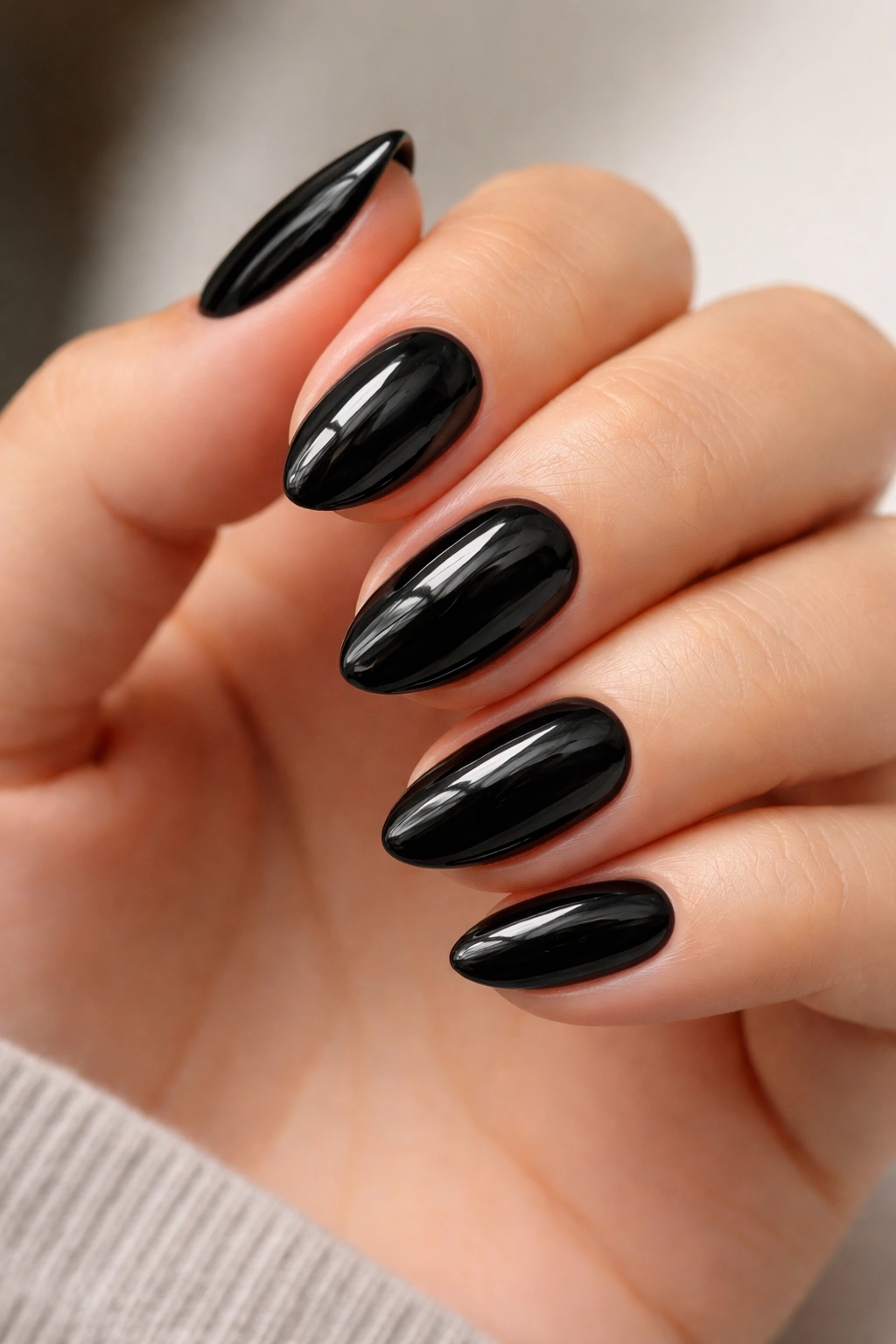 Close-up of glossy jet black short almond nails with a sharp tapered tip