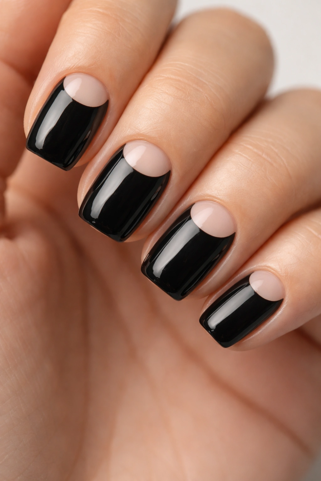 Close-up of short squoval nails with black base and crescent negative space moon shapes.