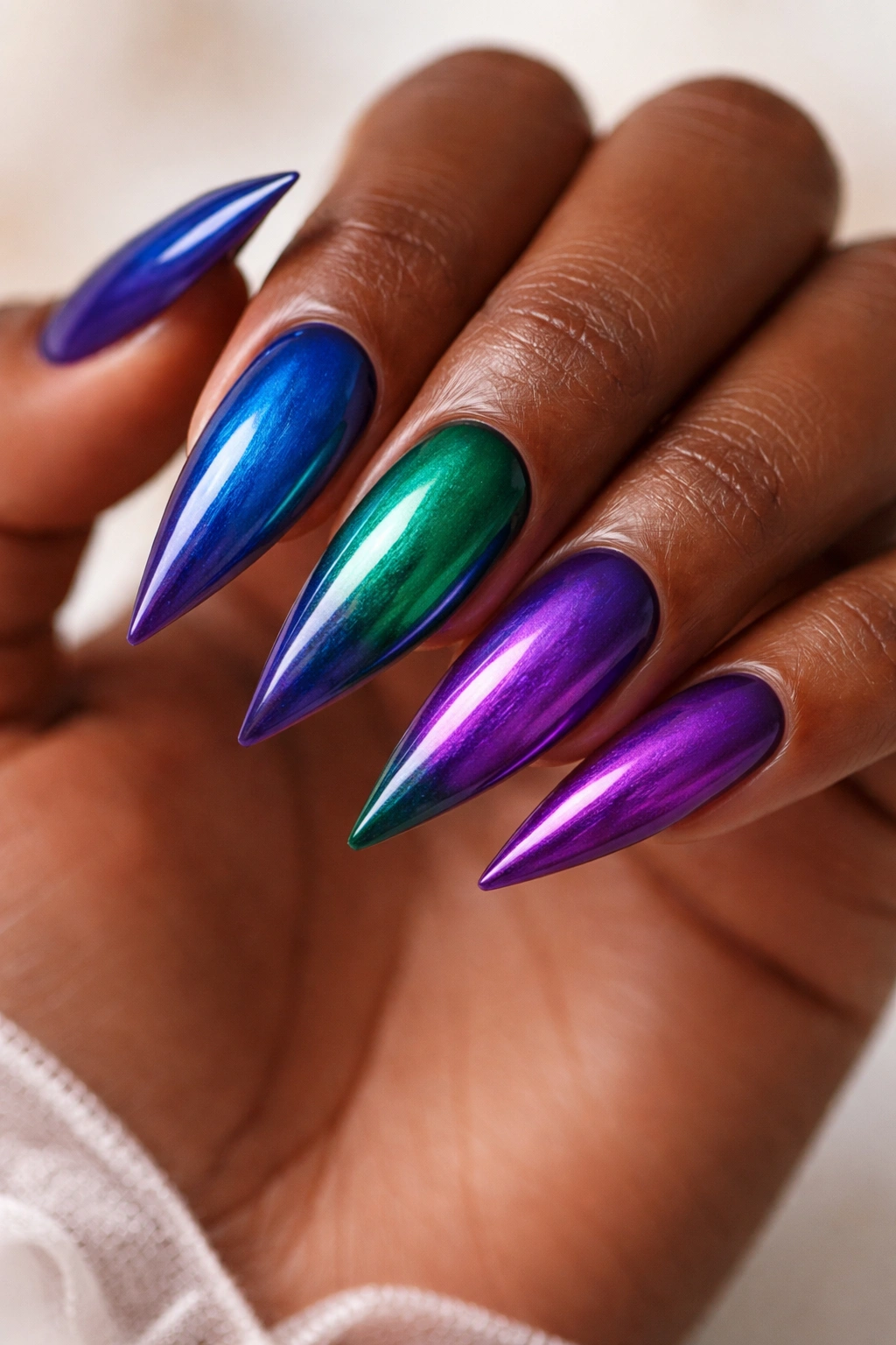 Stiletto nails in a jewel-tone gradient (sapphire, emerald, amethyst) with high gloss.