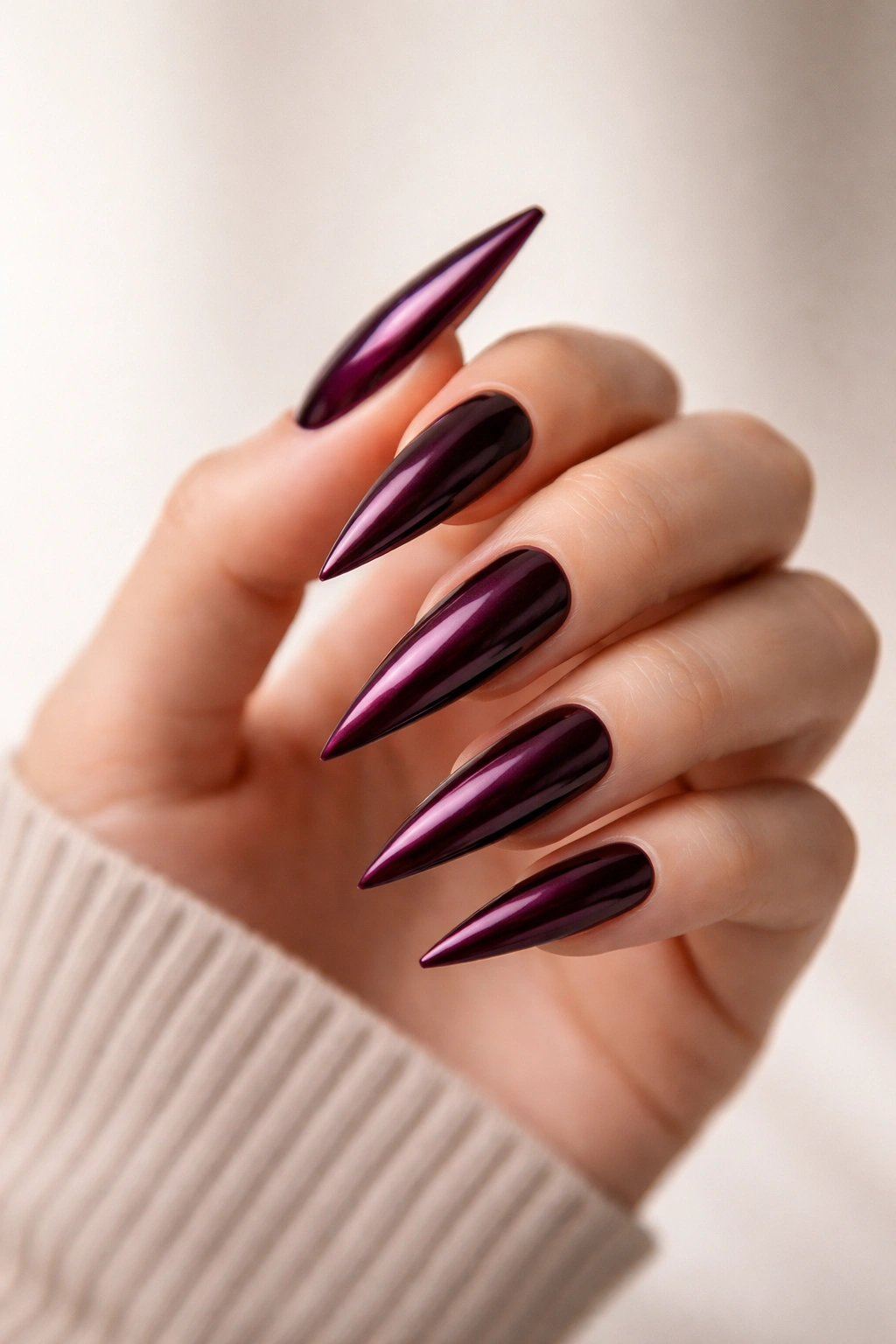 Close-up of bold jewel-toned stiletto nails on a plain background