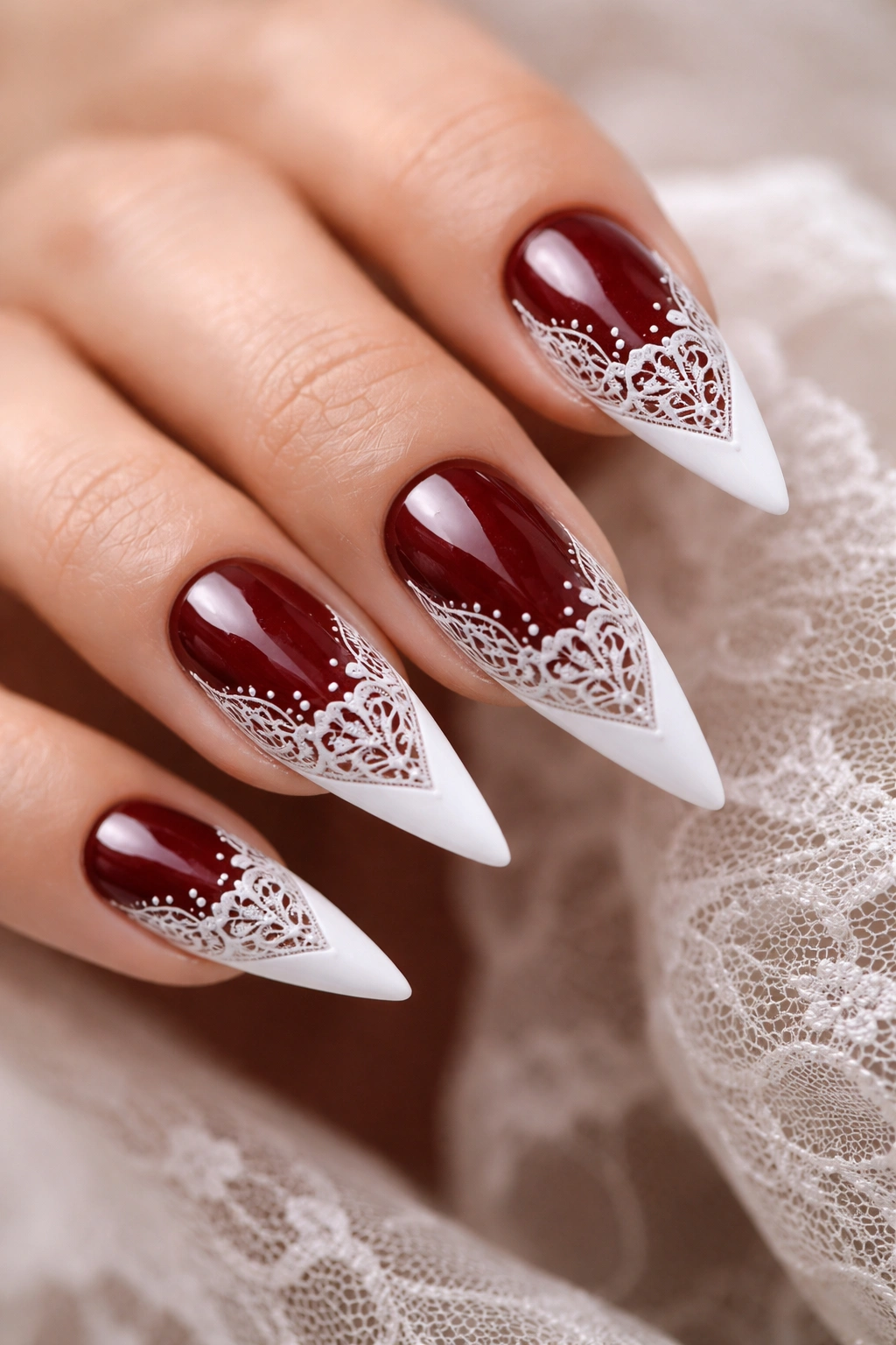 Close-up of dark red nails with white lace detailing over the tips