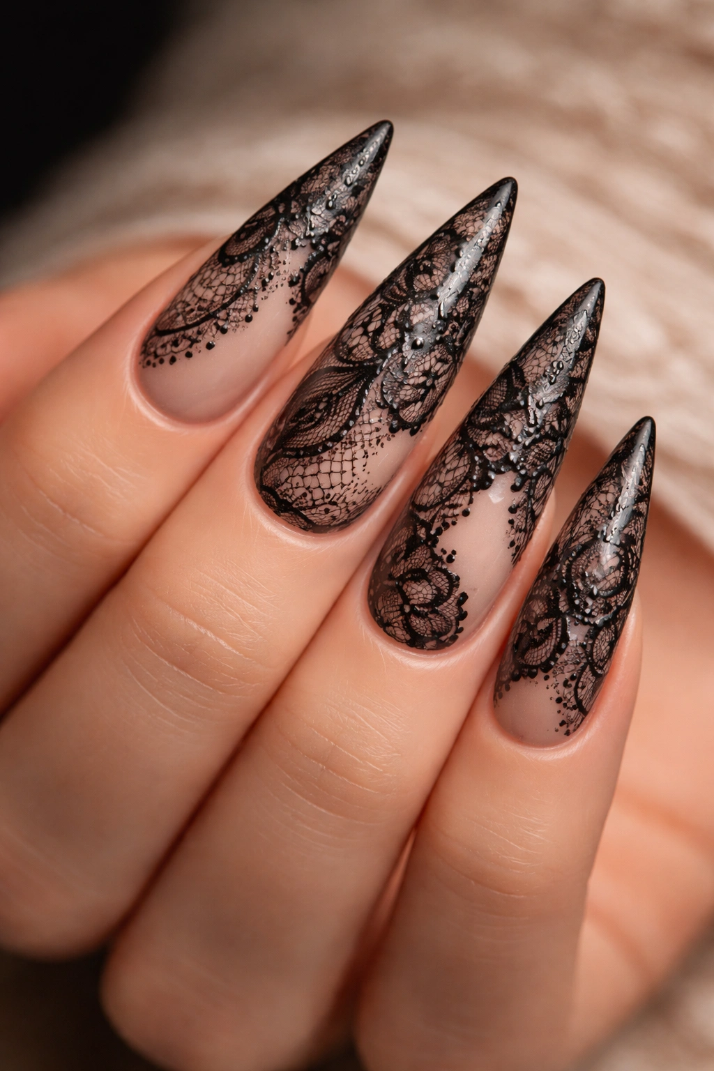 Nude stiletto nails with black lace patterns overlay.