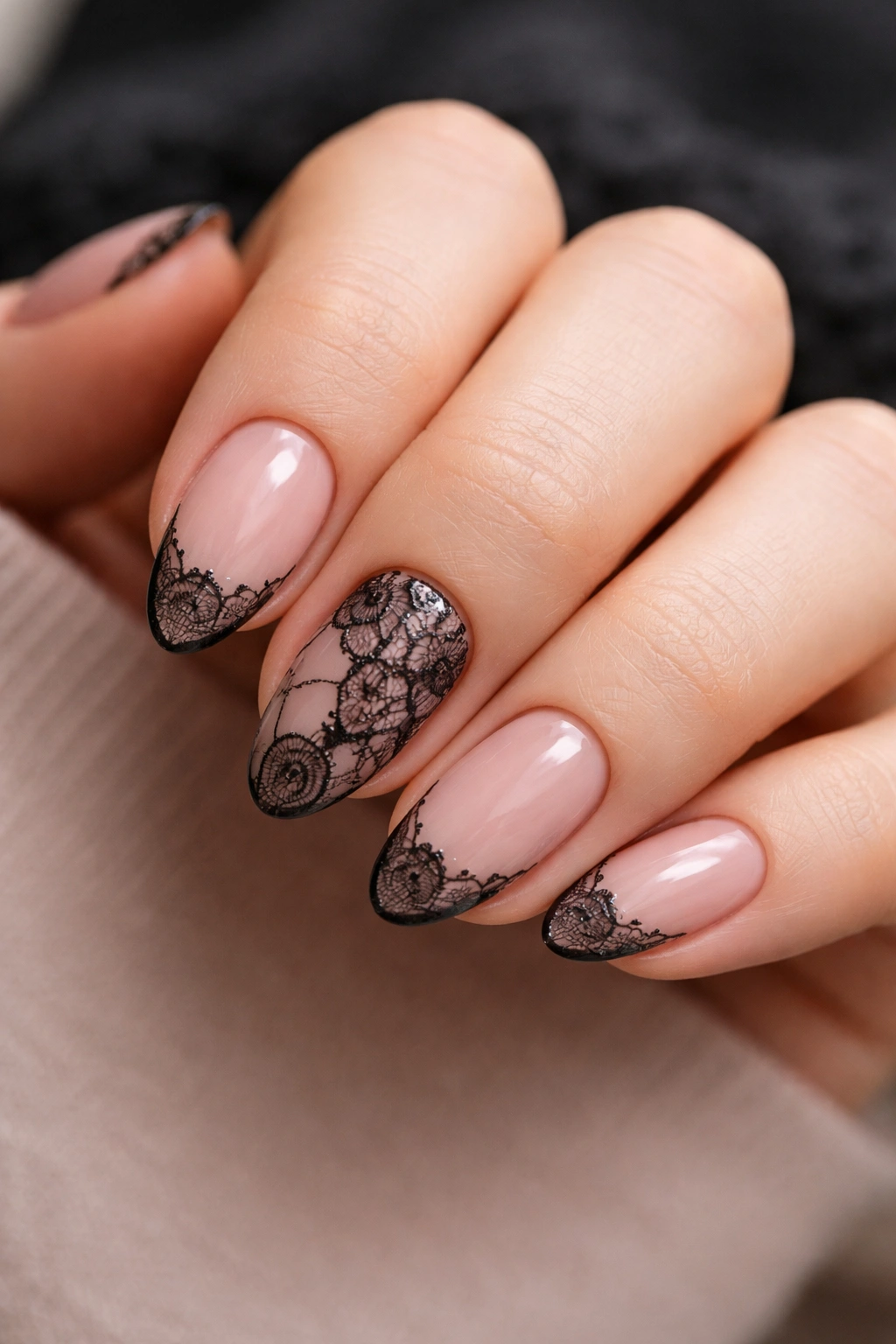 Close-up of short almond nails with delicate black lace over pale polish