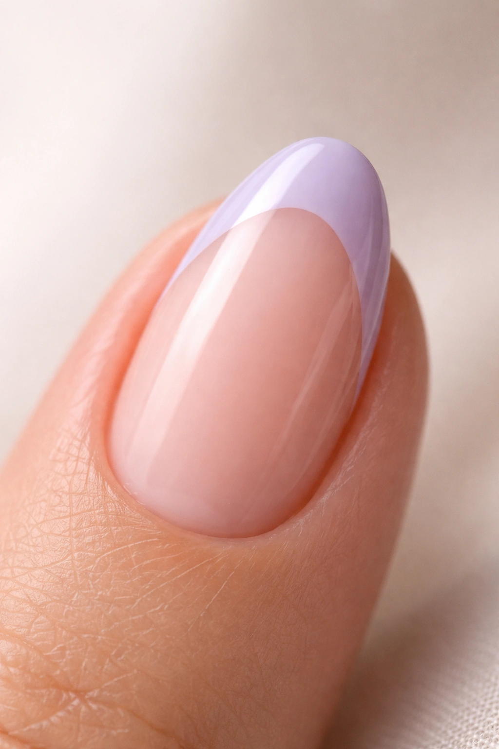 Close-up of a short almond nail with a cool greyed lavender French tip on a nude base