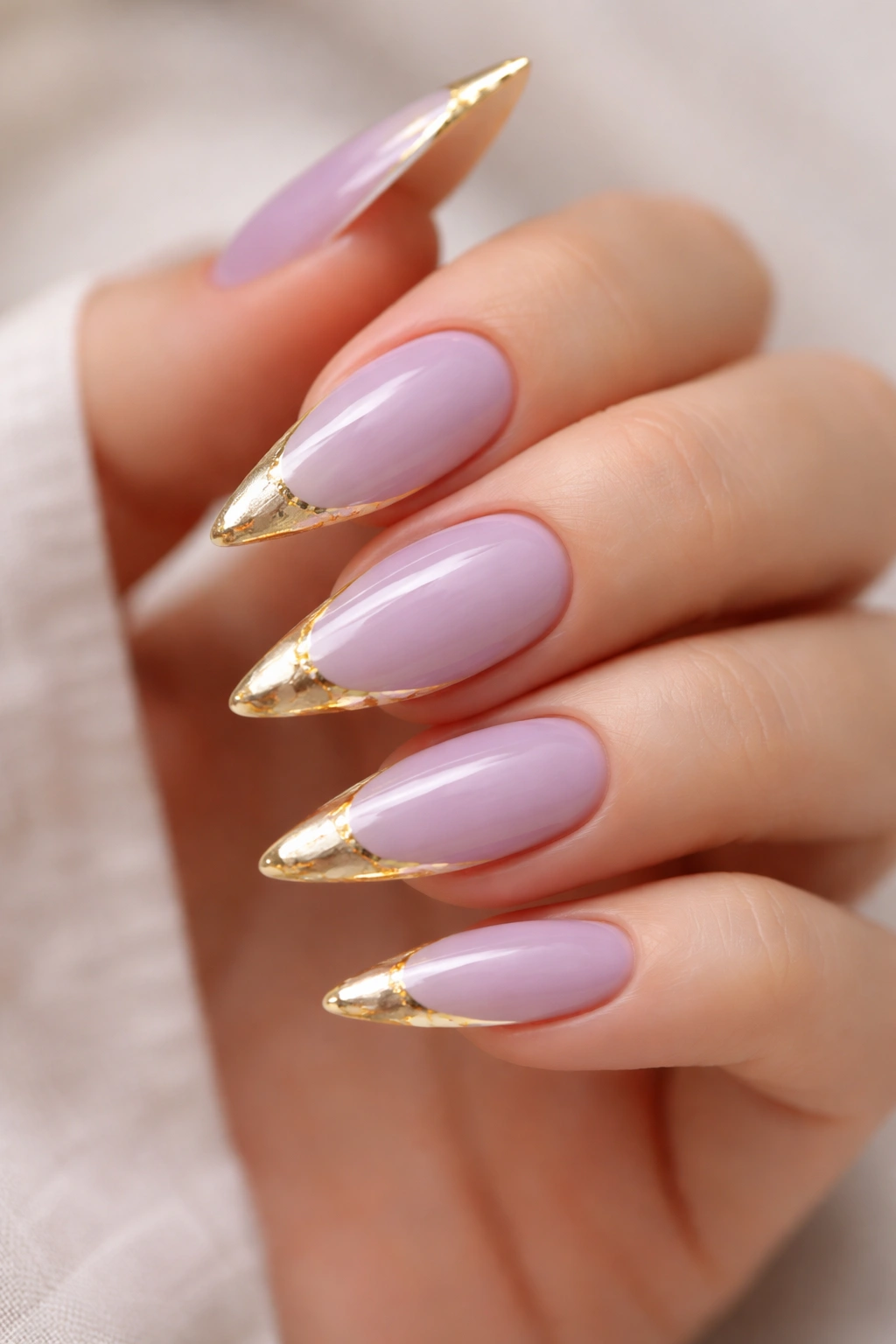 Close-up of lavender stiletto nails with white tips and a gold foil edge