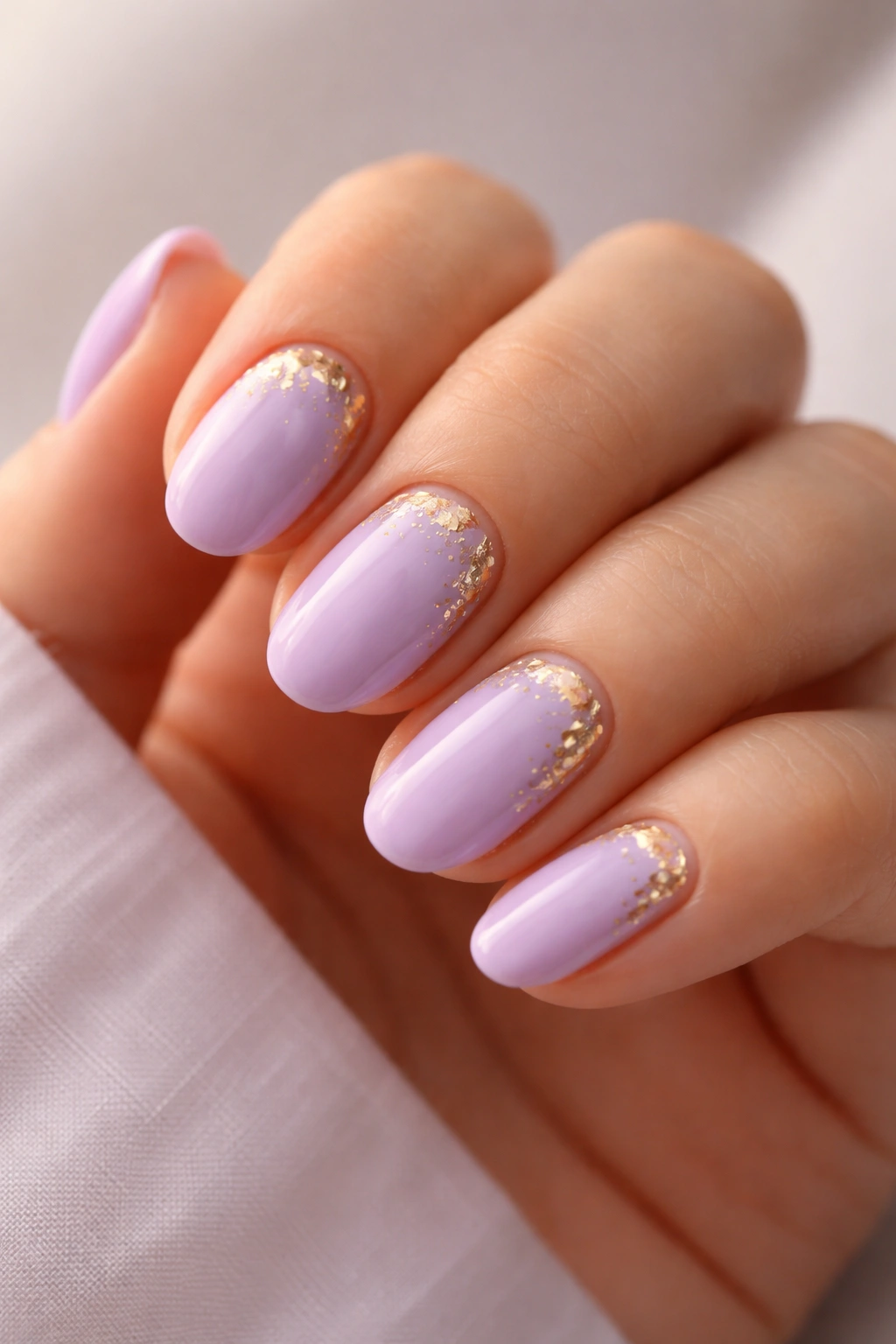 Short lavender nails with subtle gold foil accents on oval shape