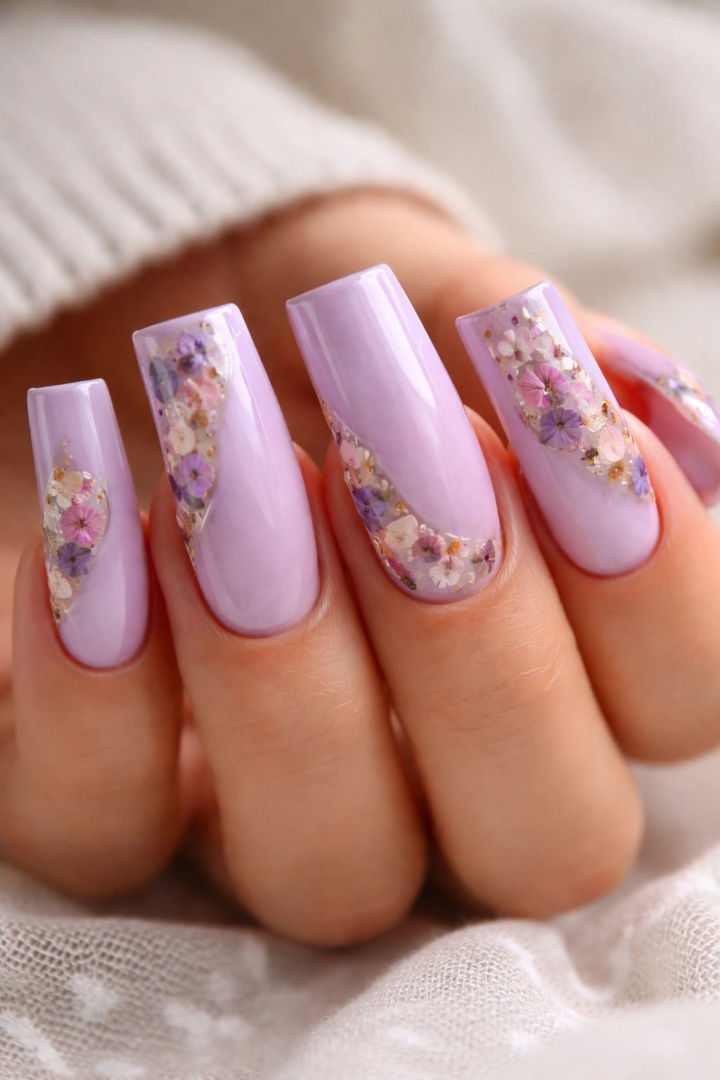 Close-up of soft lavender curved duck nails with pressed flowers under clear gel.