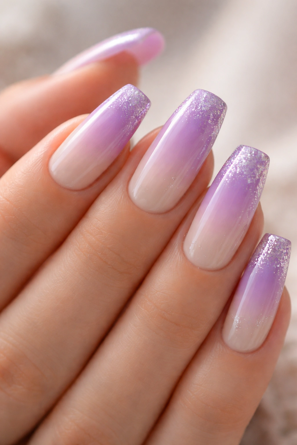 Close-up of lavender ombre coffin nails with glitter tips on a neutral studio background