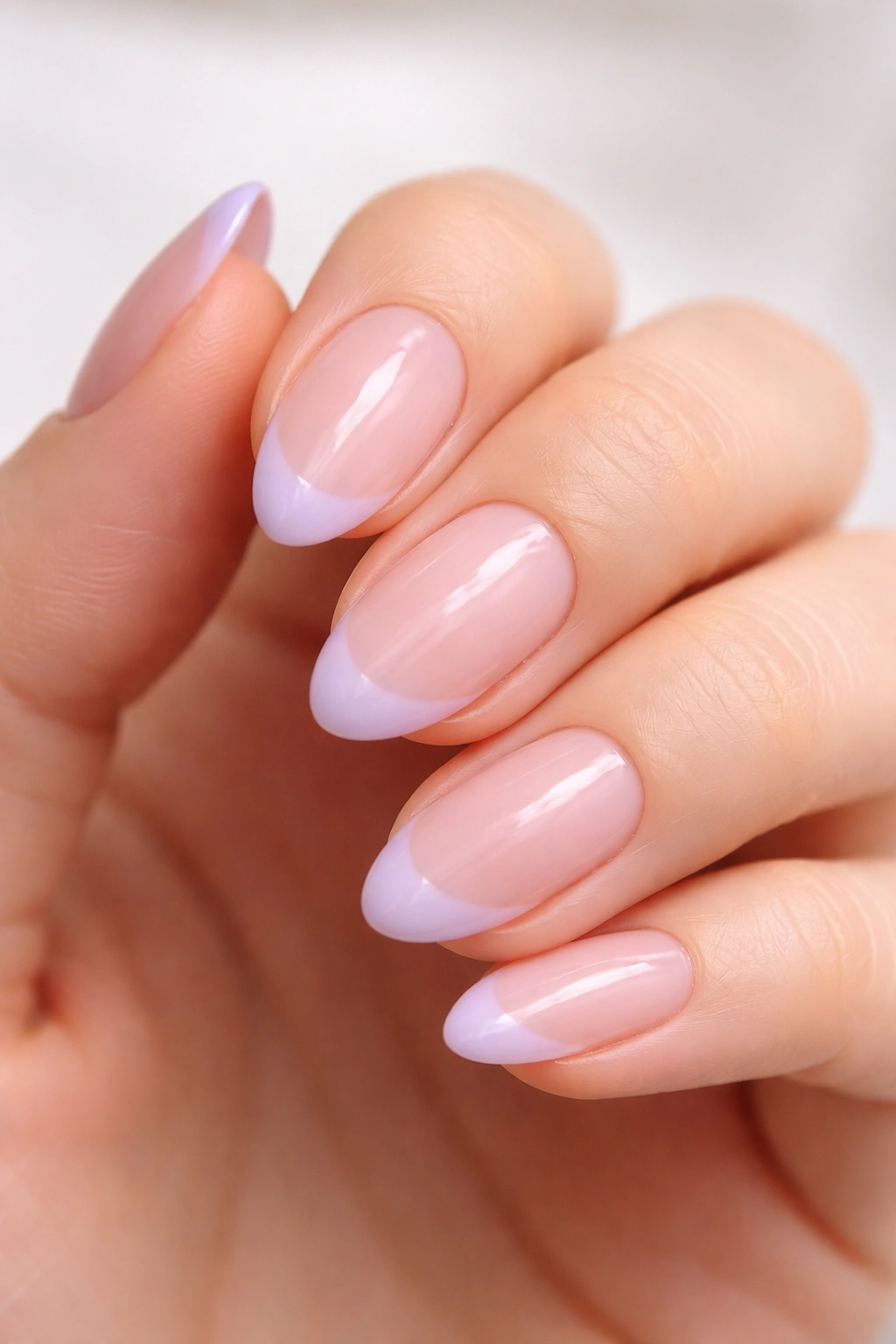 Close-up of short almond nails with sheer pink base and pale lavender tips