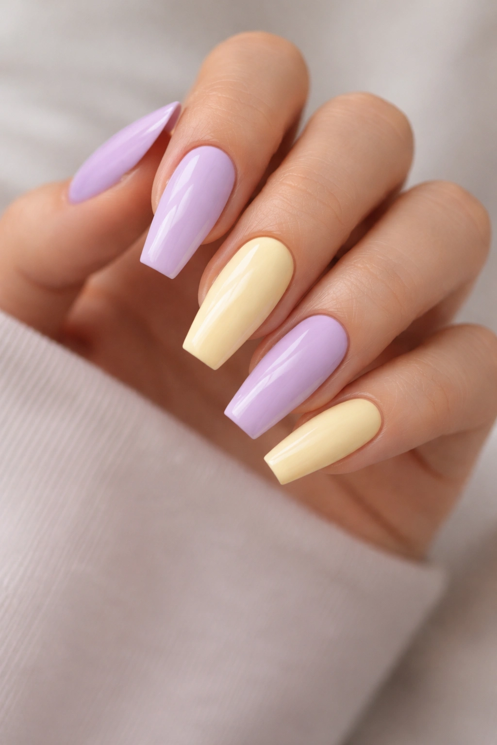 Hand showing alternating lemon and lavender nails in soft pastels