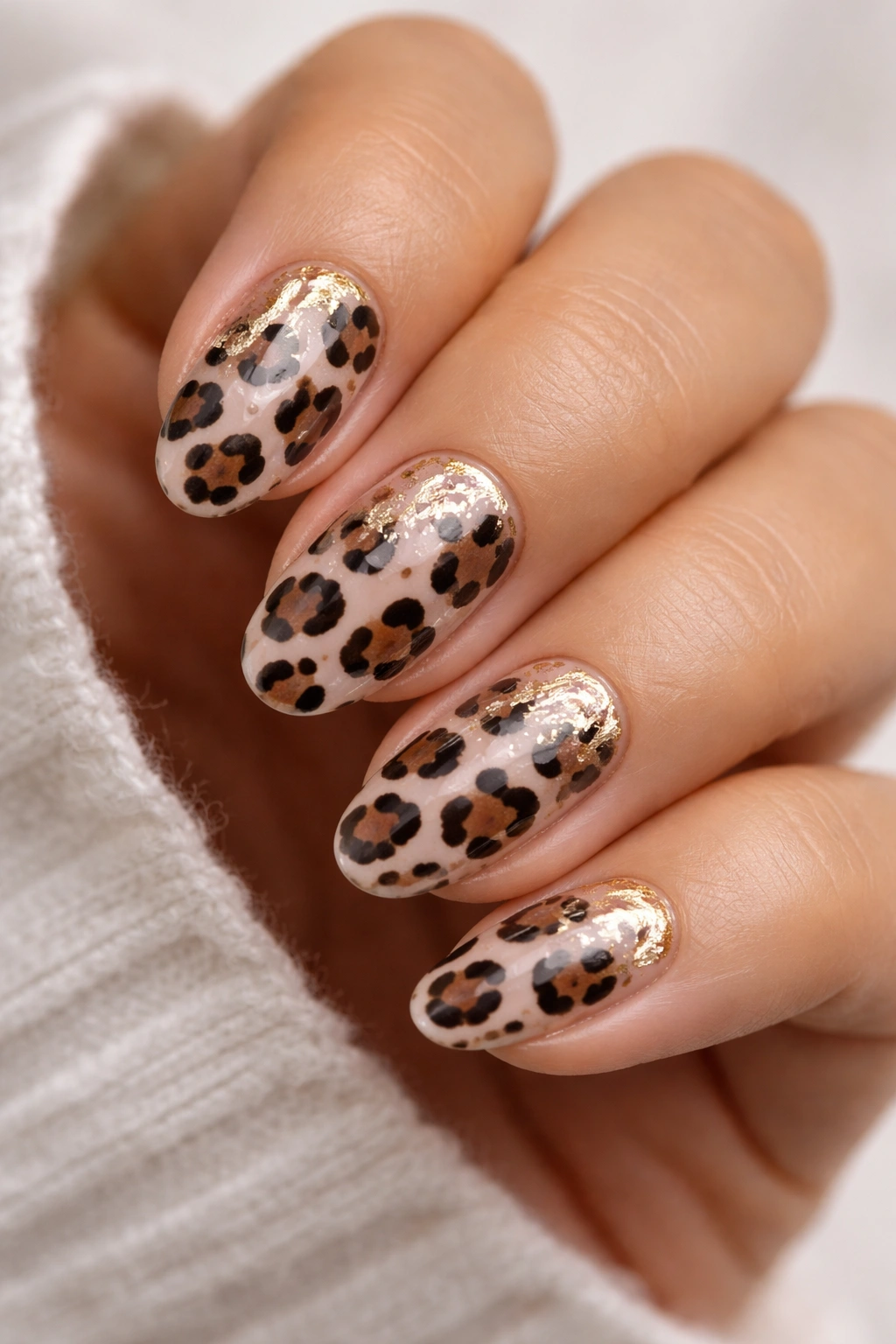 Close-up of short almond nails with leopard print and gold foil flecks