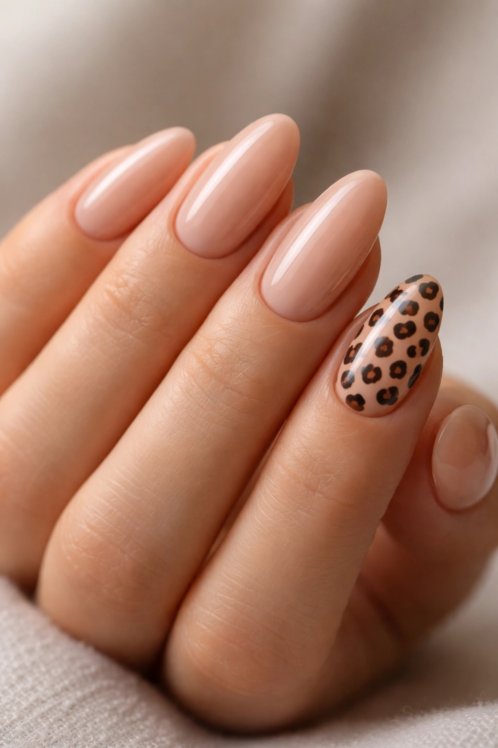 Close-up of a hand with one leopard-print nail among nine glossy nude nails