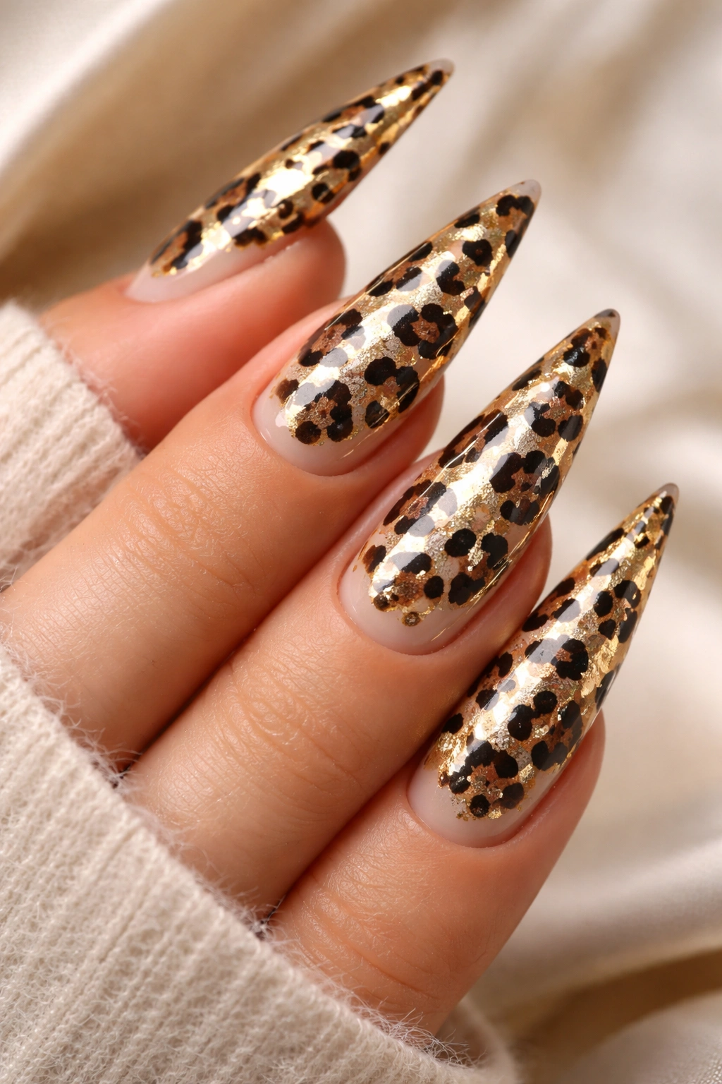 Nude stiletto nails featuring leopard print with gold foil accents