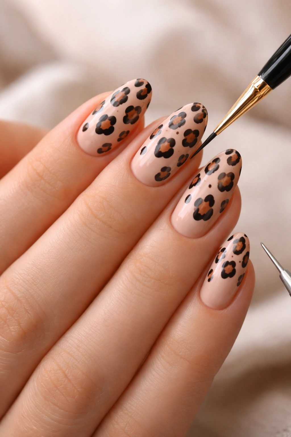 Close-up of hands painting leopard print on short almond nails with a fine brush