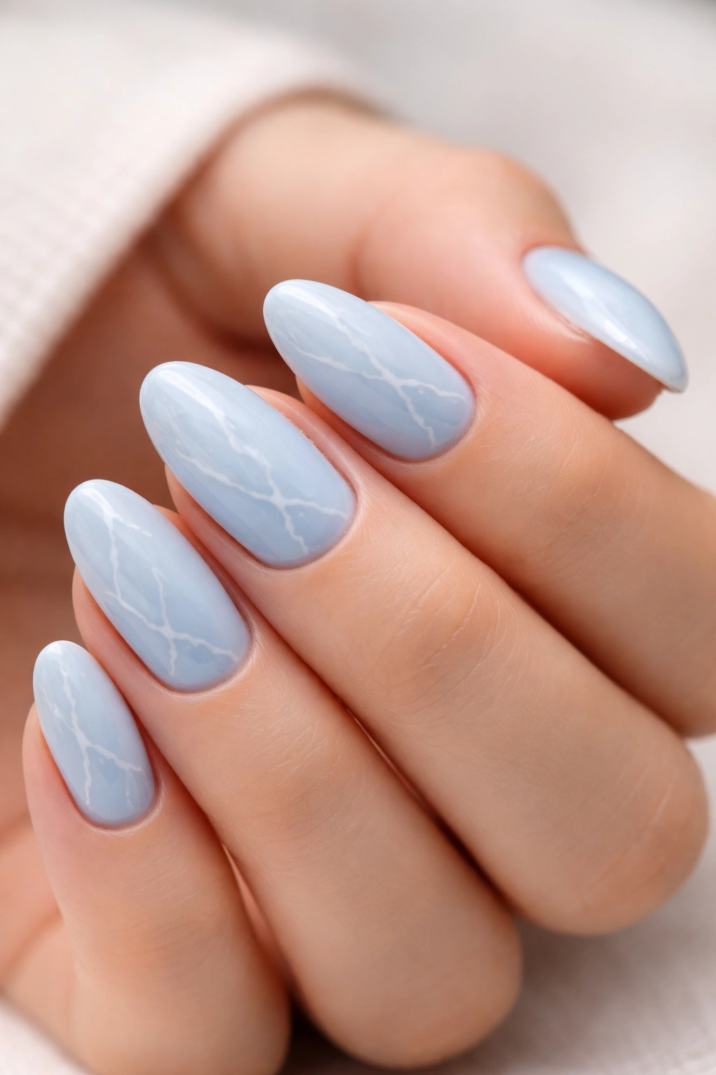 Short almond nails with light blue base and thin white marble veins
