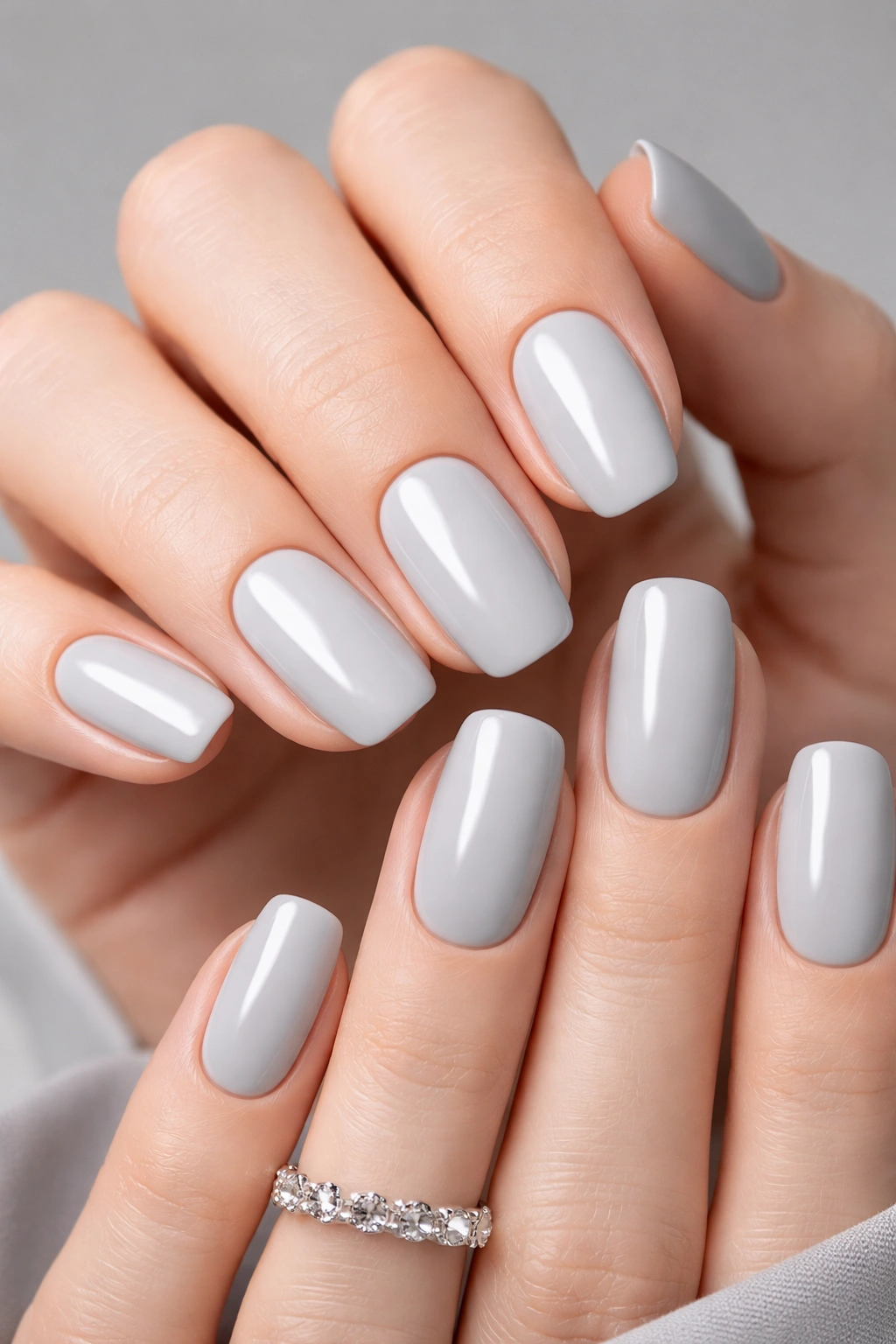 Close-up of light gray manicured nails with glossy finish in a neutral studio setting