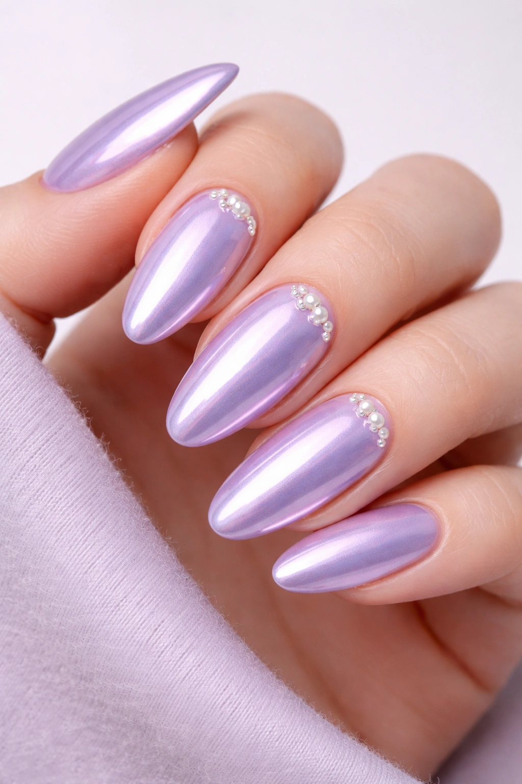 Close-up of light purple chrome nails with small pearl accents near the cuticle