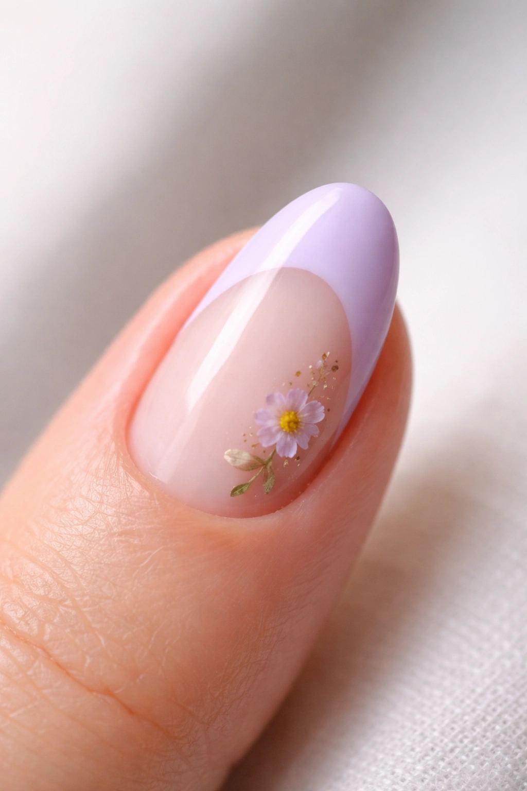 Close-up of a short almond nail with lilac tip and pressed flower accent at the base