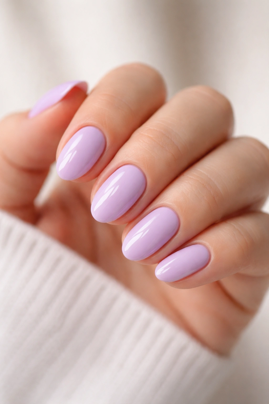 Close-up of short almond nails painted creamy lilac with glossy finish
