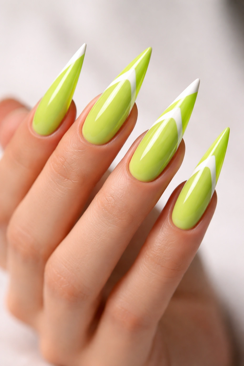 Lime green stiletto nails with diagonal neon tips in a French manicure style