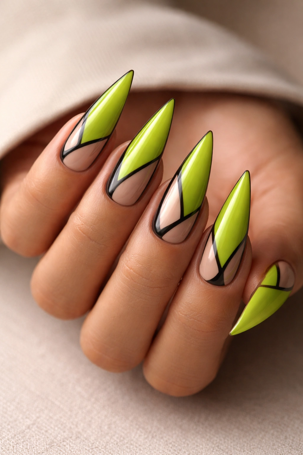 Close-up of lime green stiletto nails with black negative-space shapes on a neutral background