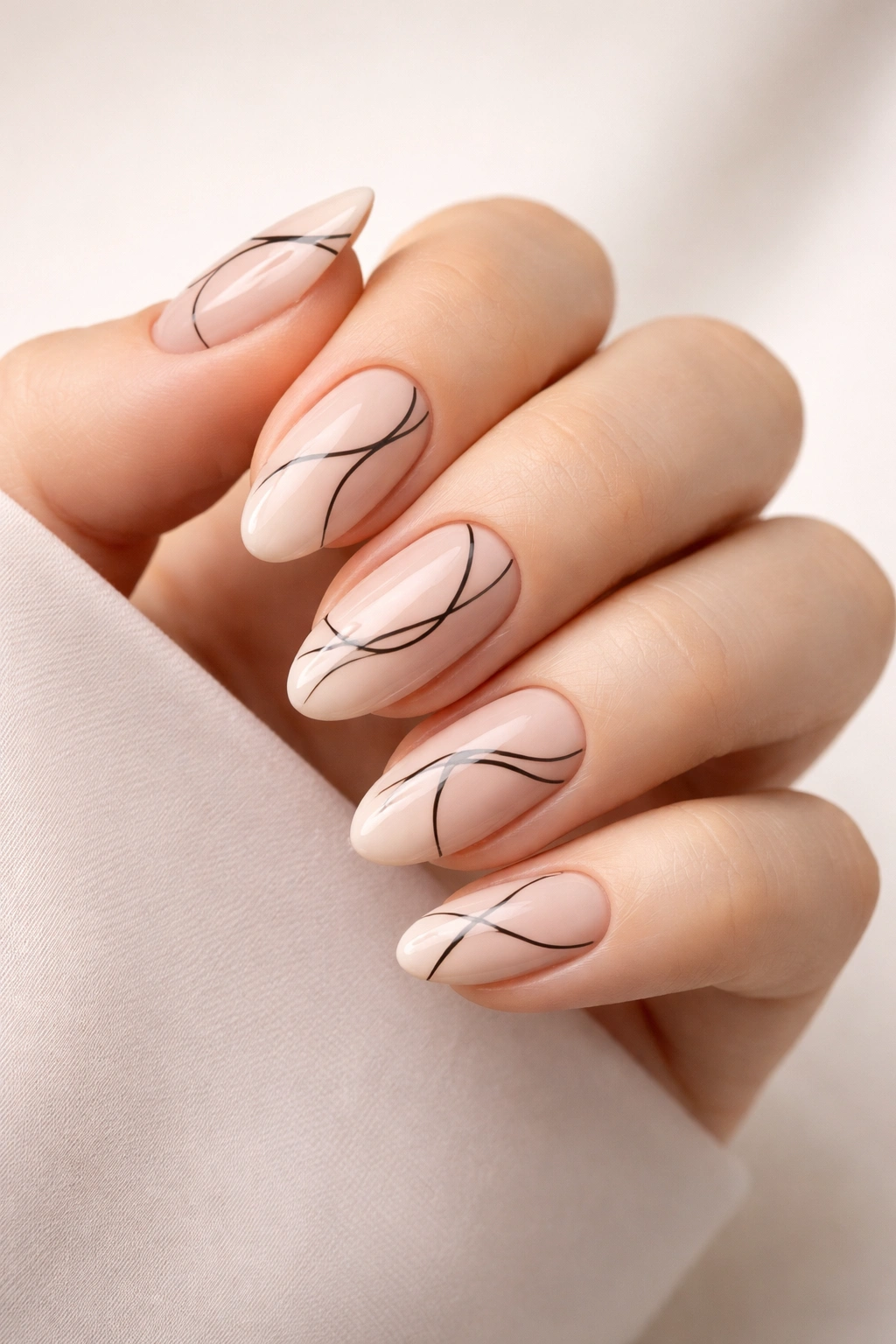 Close-up of almond nails with minimalist black line art on nude base