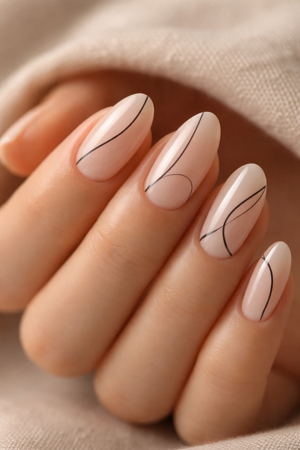 Close-up of minimal line art on short almond nails with nude base.
