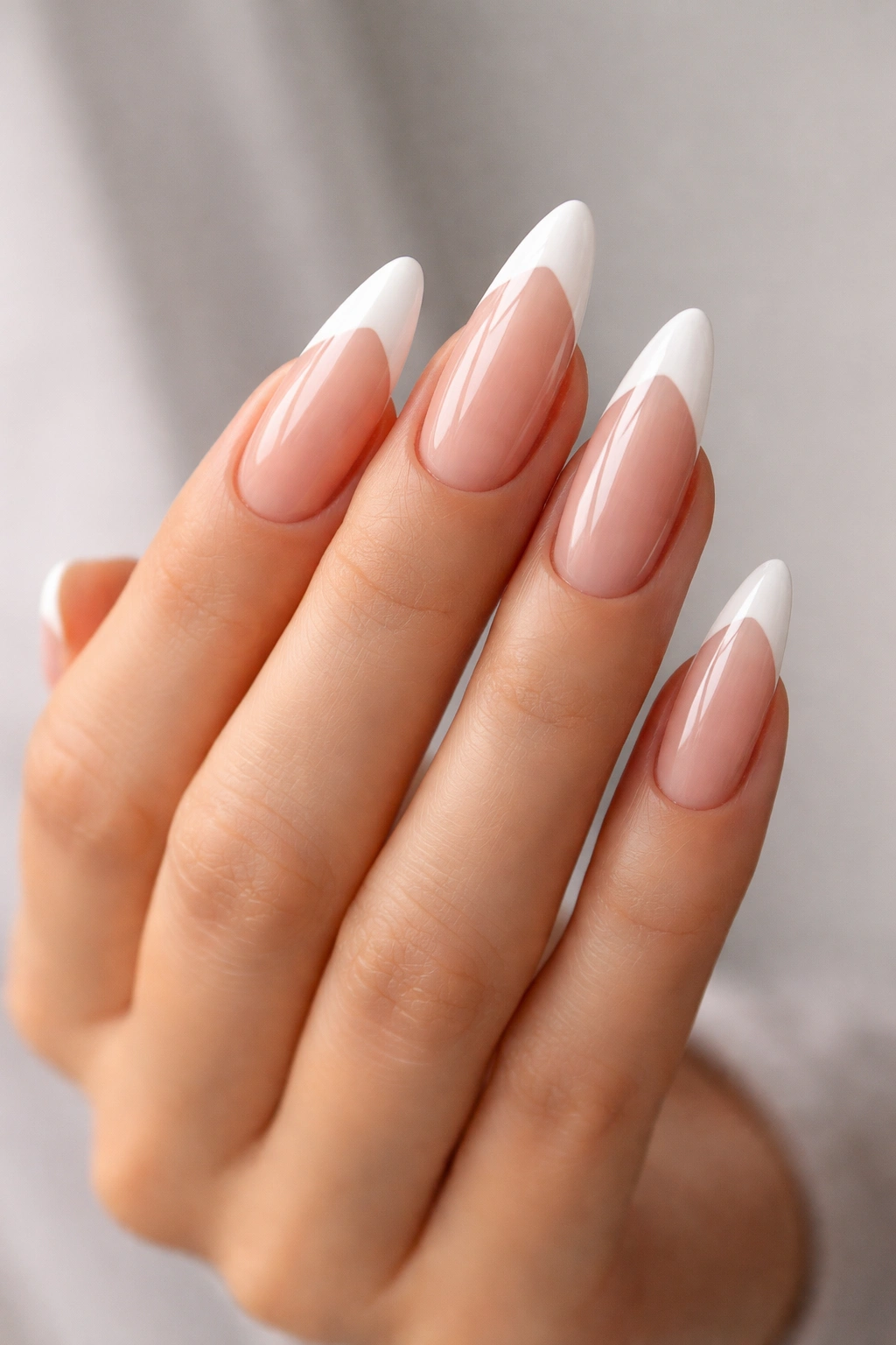 Close-up of long almond nails with subtle diagonal white tips on a neutral background