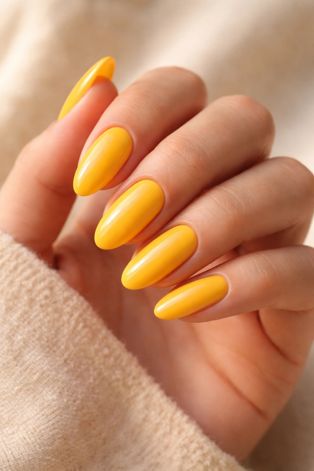 Close-up of long oval nails painted mango yellow with creamy finish on bare hand