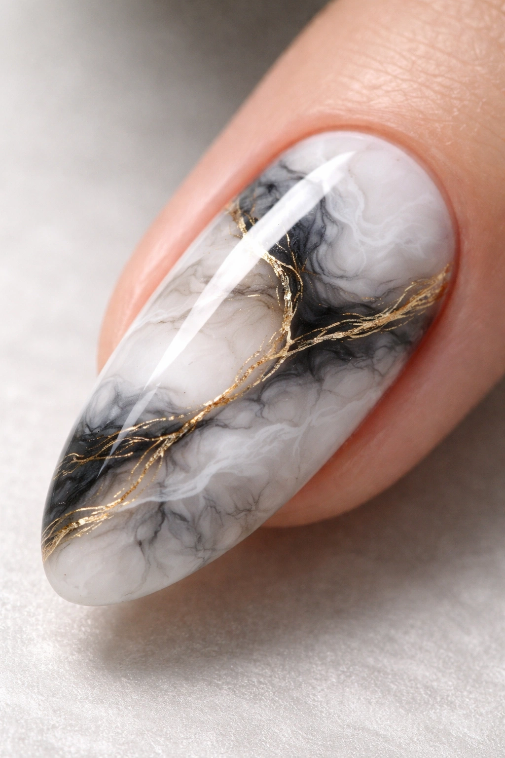 Close-up of marble-effect blooming gel nail with white, gray, and gold veining