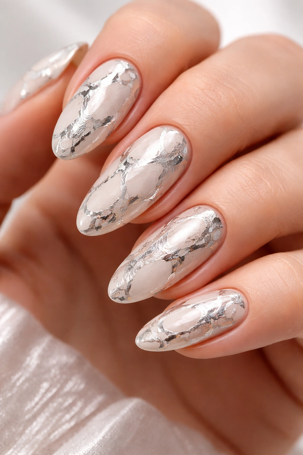 Nails with white/nude base and irregular silver foil veining like marble.