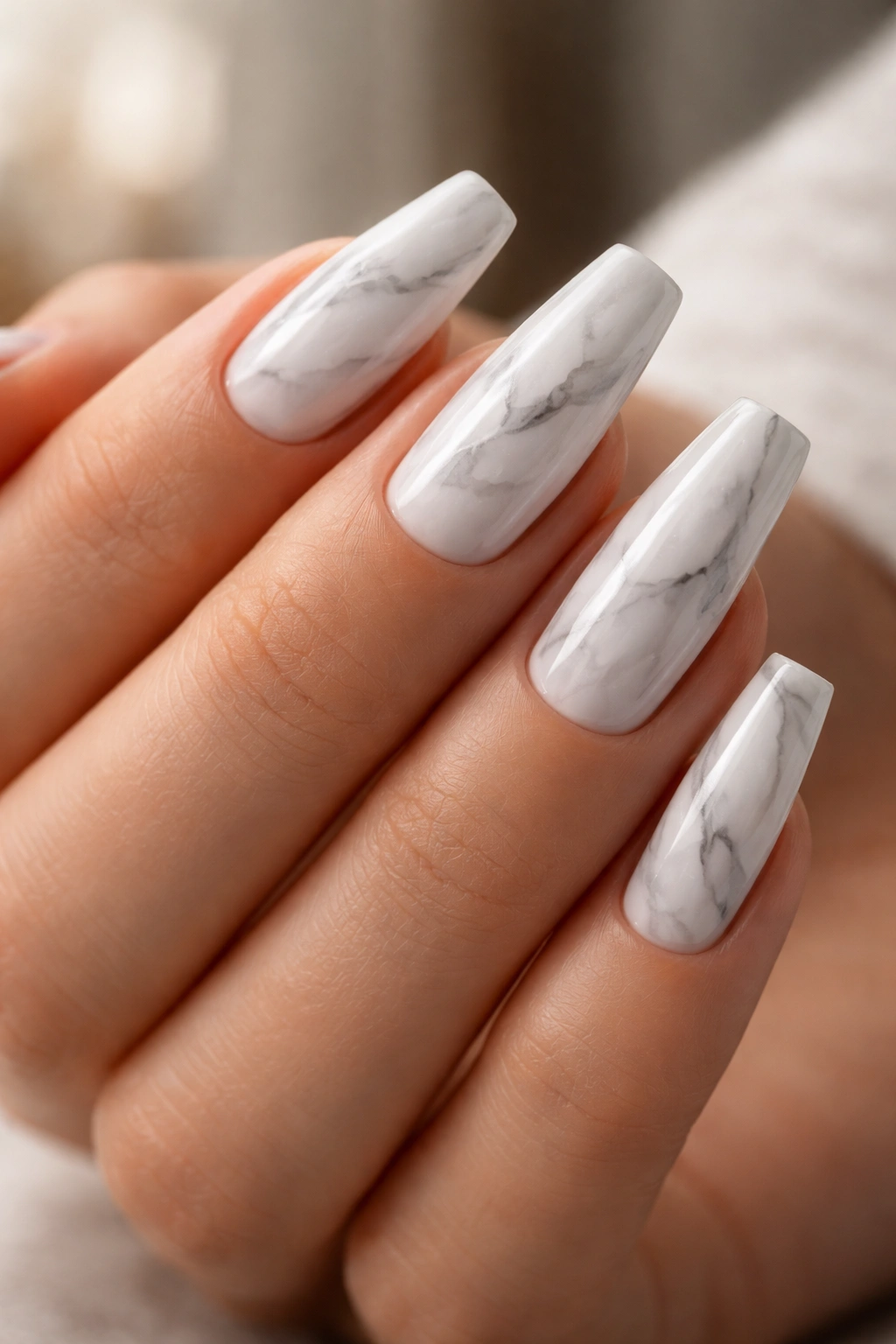 Close-up of marble nails in a ballerina shape with subtle gray veining on a white base