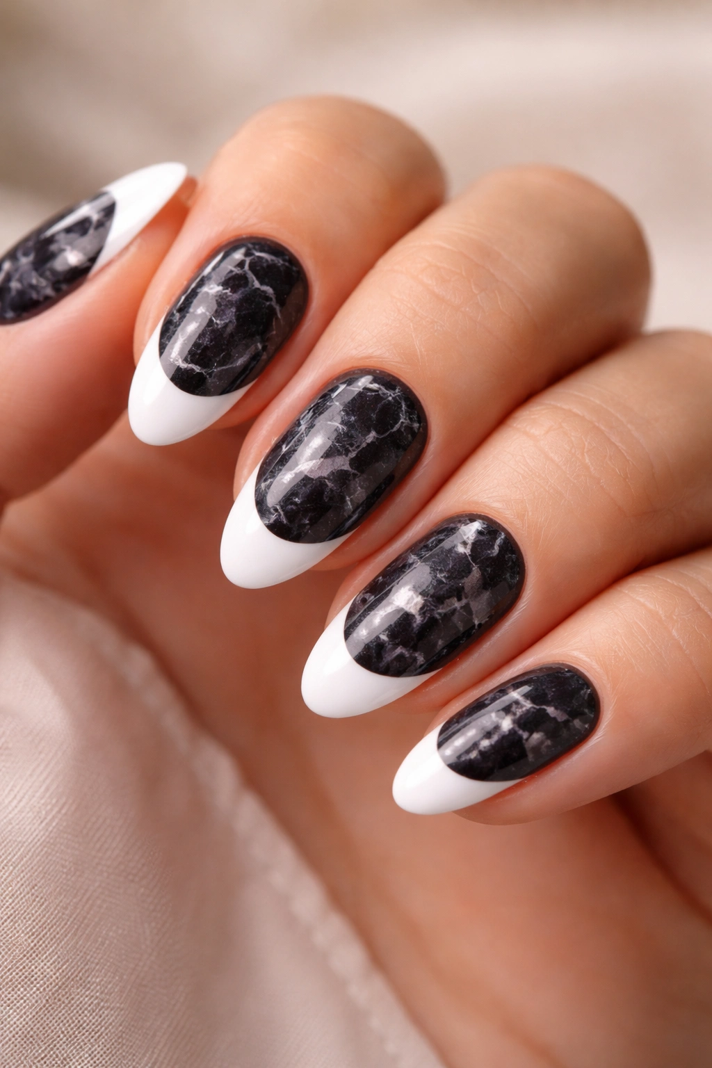 Marbled black base on short almond nails with white tip.