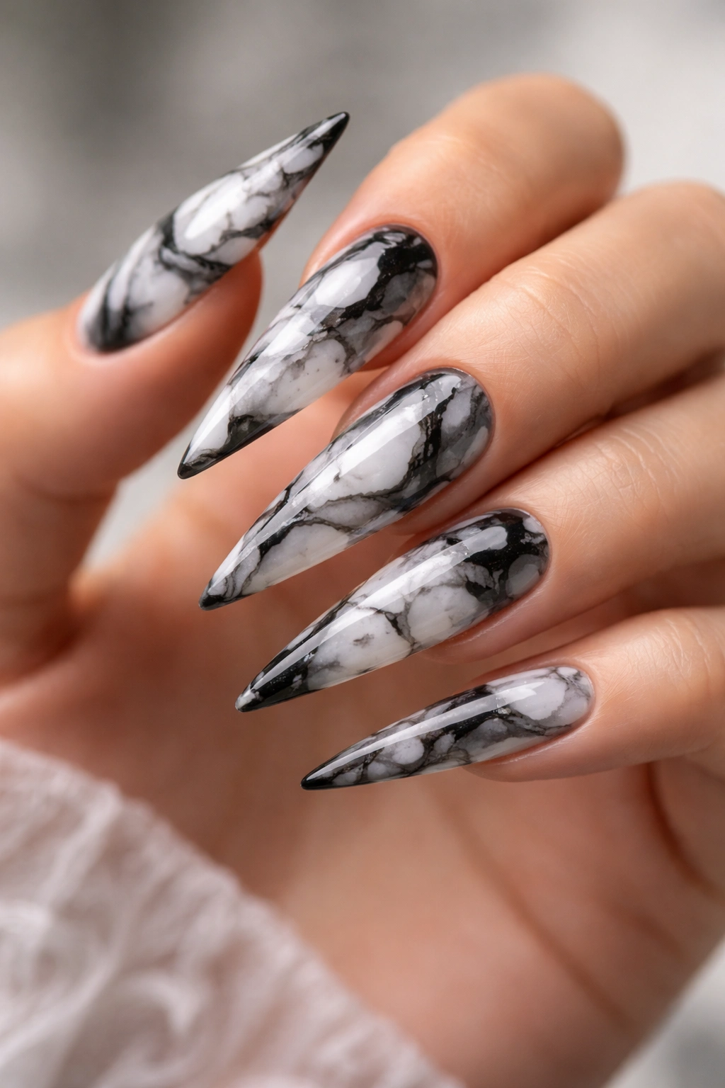 Close-up of black-and-white marble patterned stiletto nails with a glossy finish.