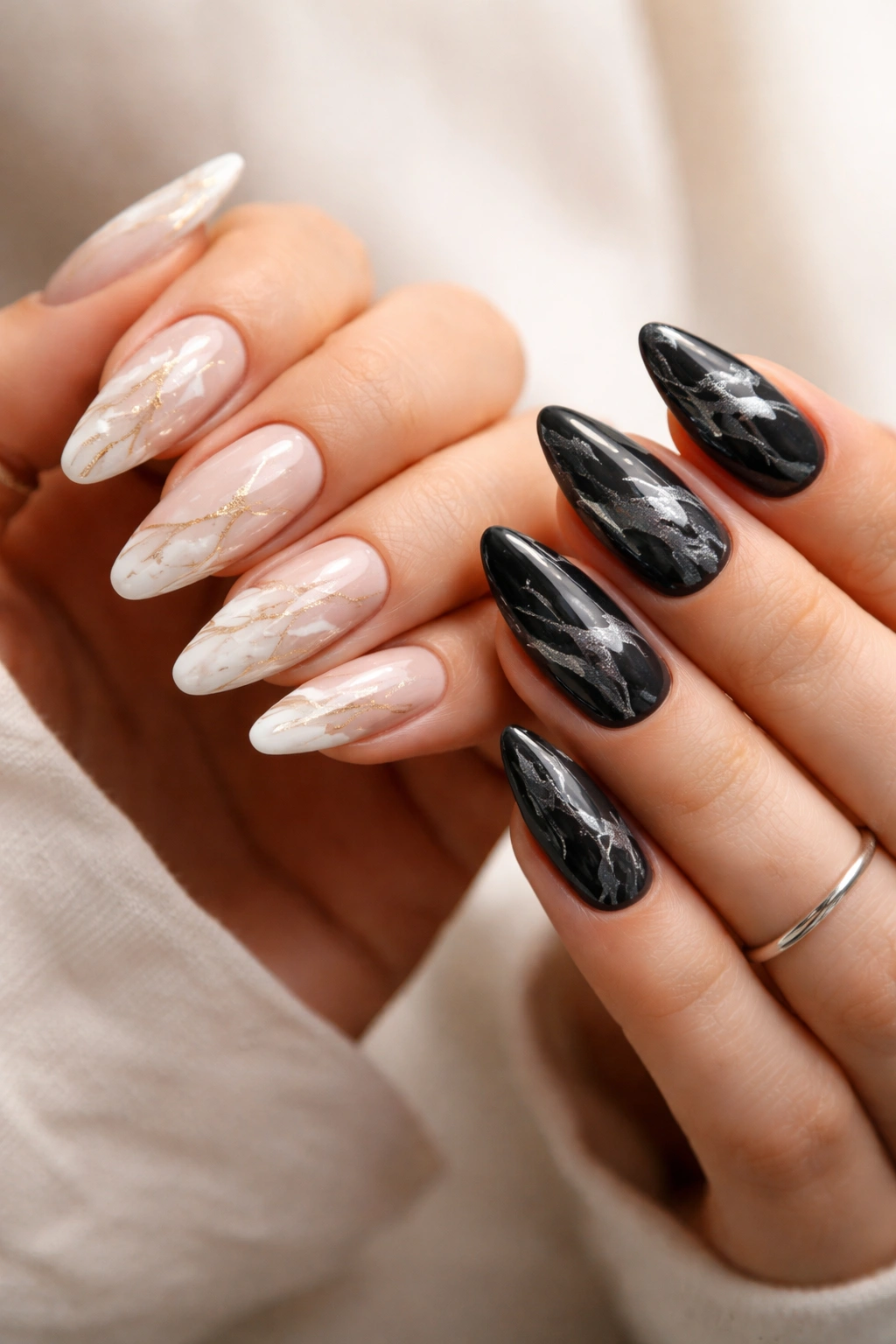 Hands with contrasting marble nail designs in white-gold and black-silver veining.