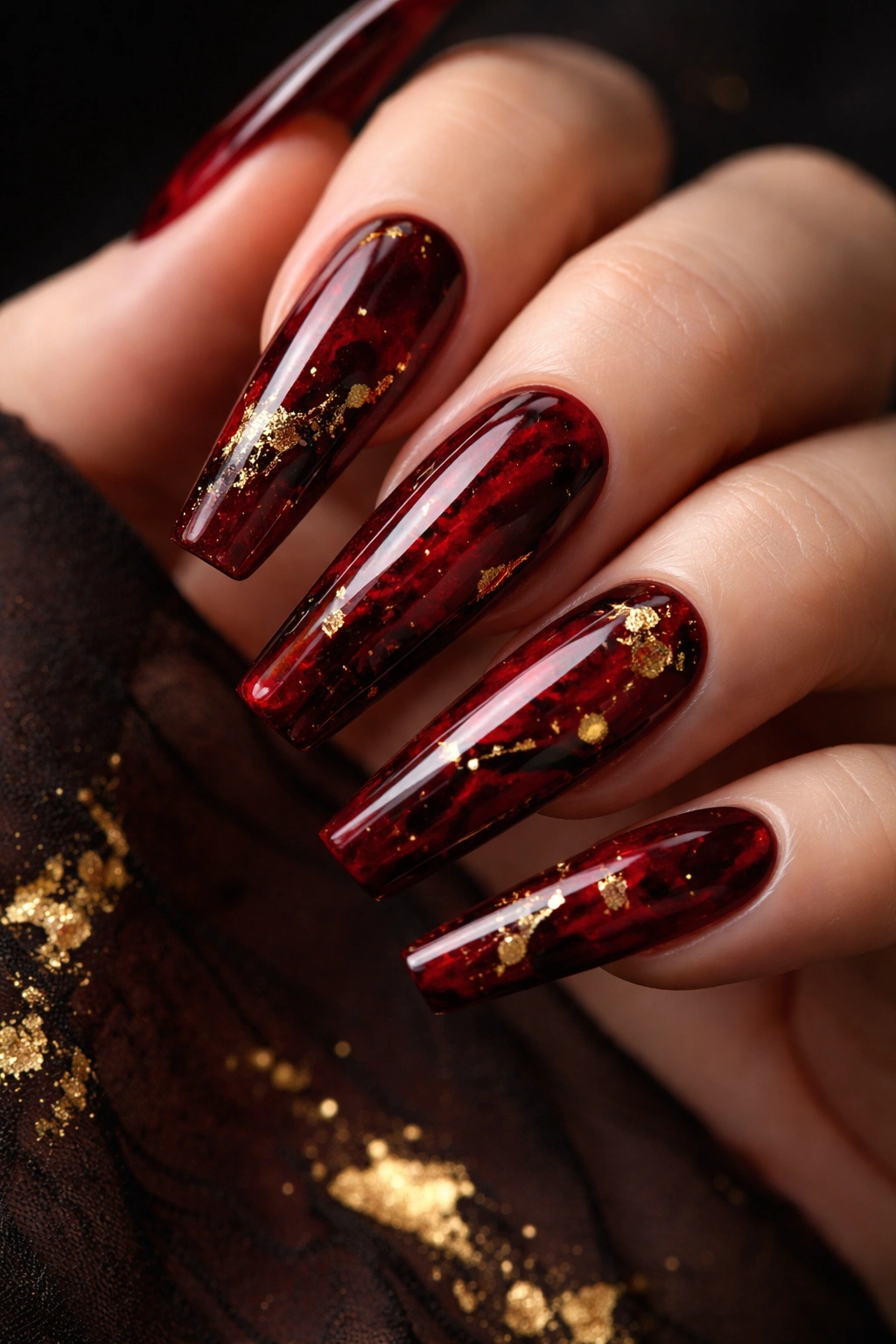 Close-up of deep red marble coffin nails with black veining and gold leaf on a dark background.