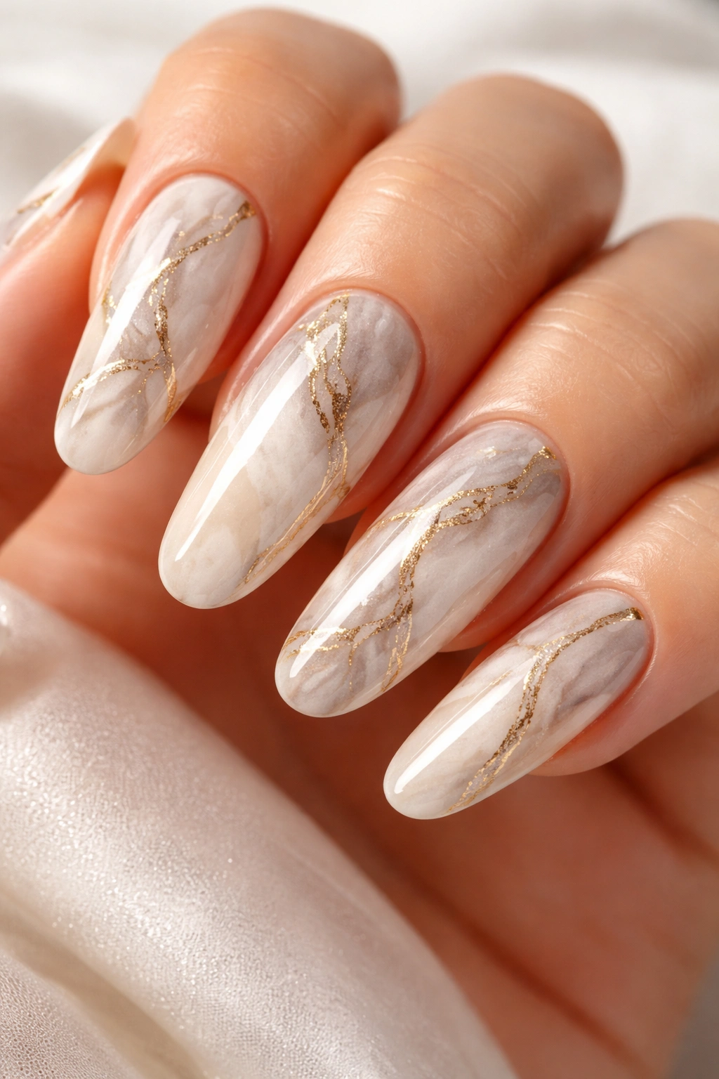 Close-up of long round acrylic nails with white-gray marble and gold veins