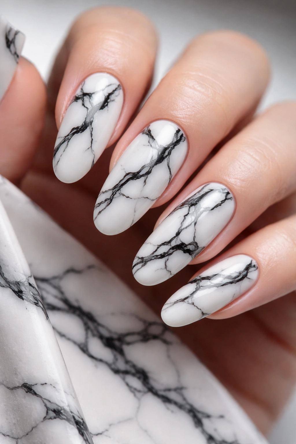 Close-up of long round nails with black veining on a white marble base
