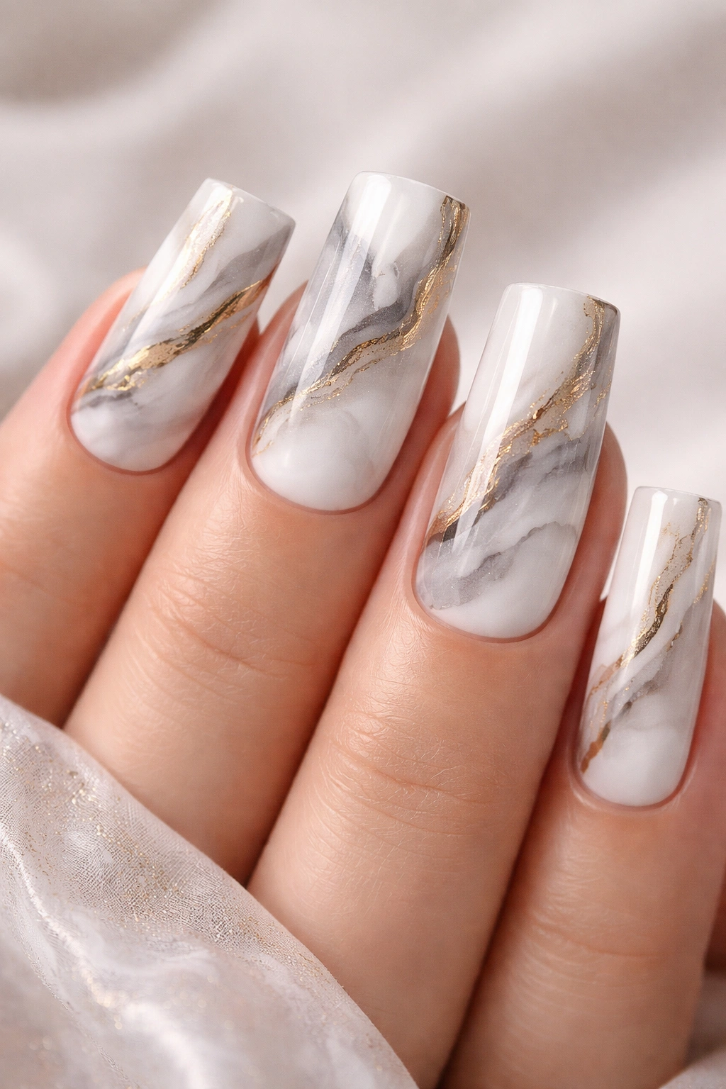 Close-up of square nails with white and gray marble veining and gold accents