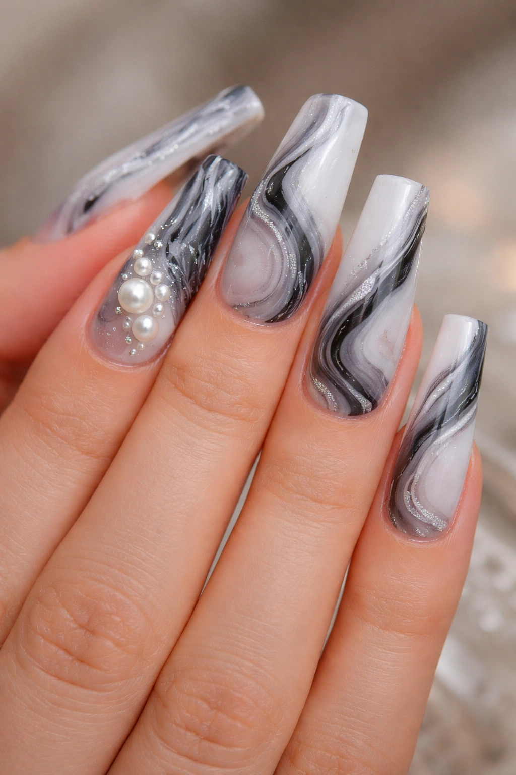Marble pattern coffin nails with pearl accents on a bare hand