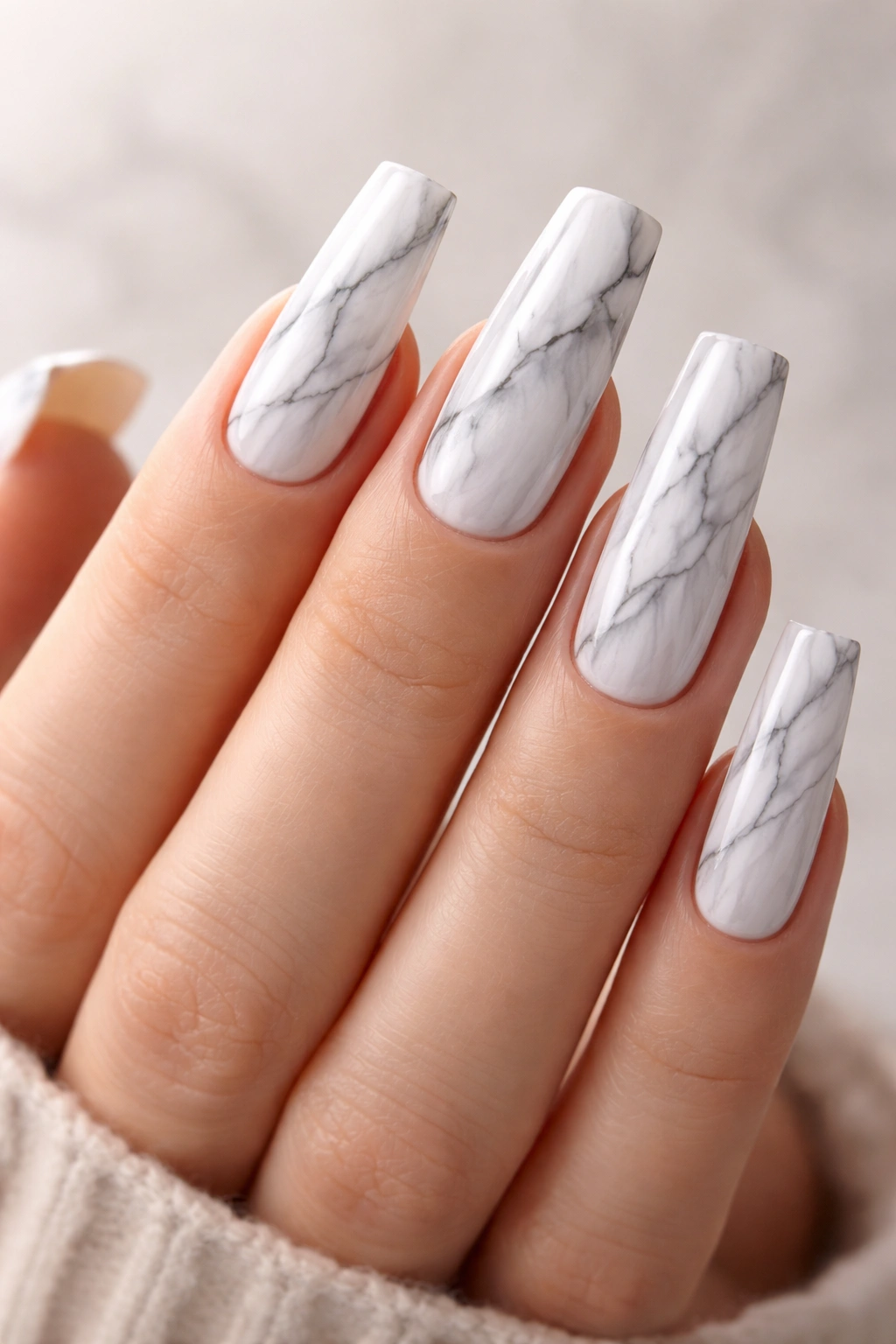 Close-up of long square nails with white-gray marble veining along their length