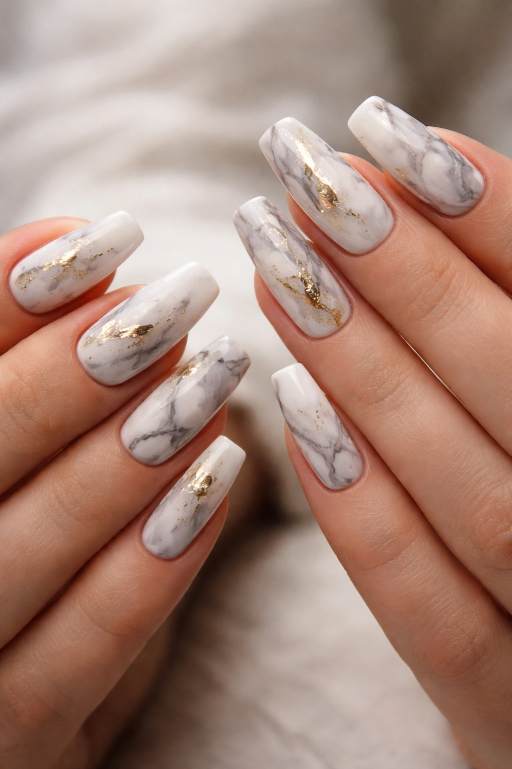 Two hands with marble nails white and gray with gold accents