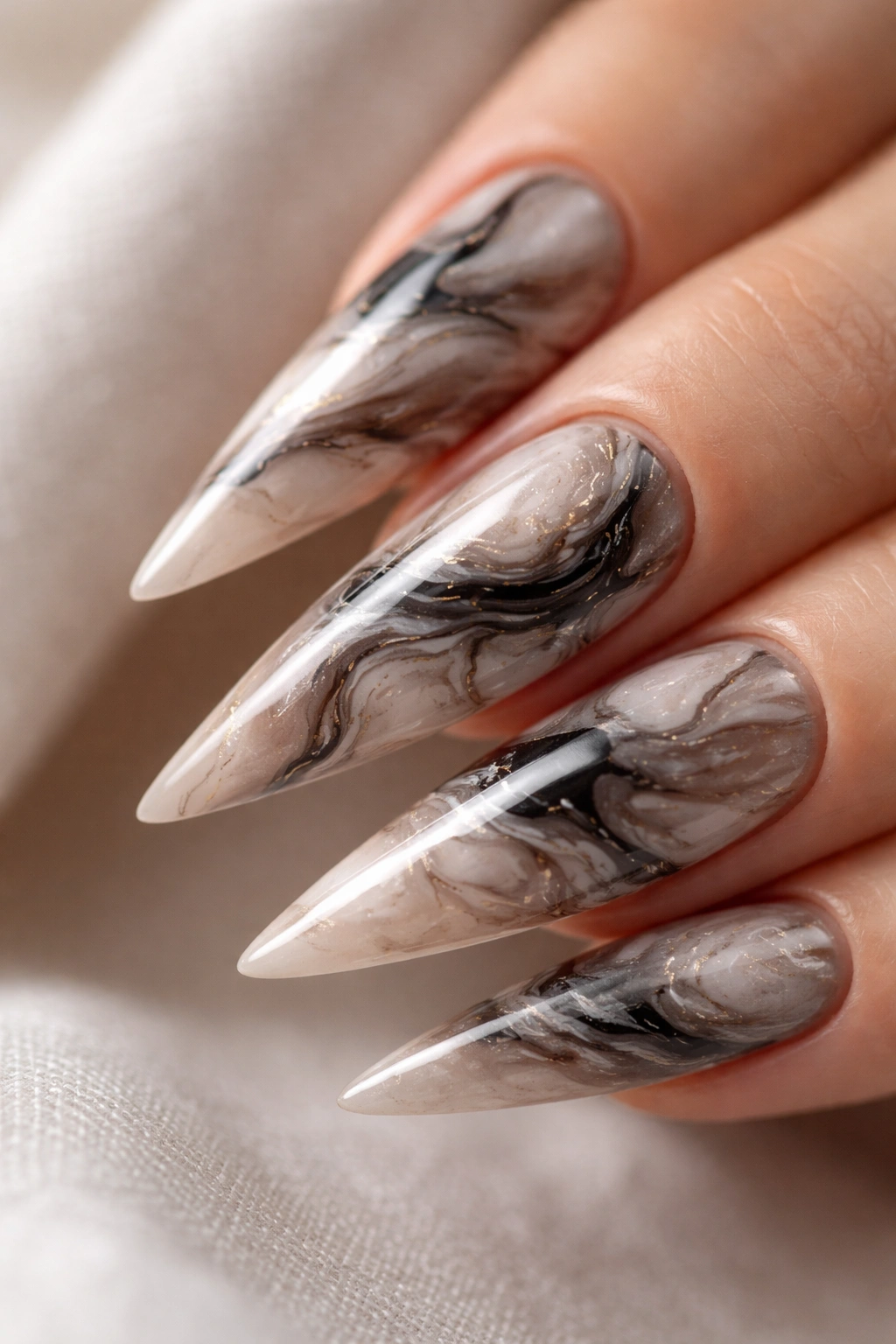 Close-up of a stiletto nail with abstract marble swirls in black, gray, white and taupe.