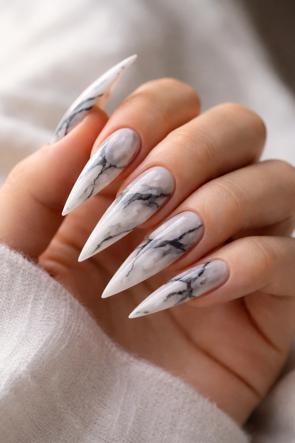 Close-up of marble-effect stilettos nails with veining on a nude base in studio lighting