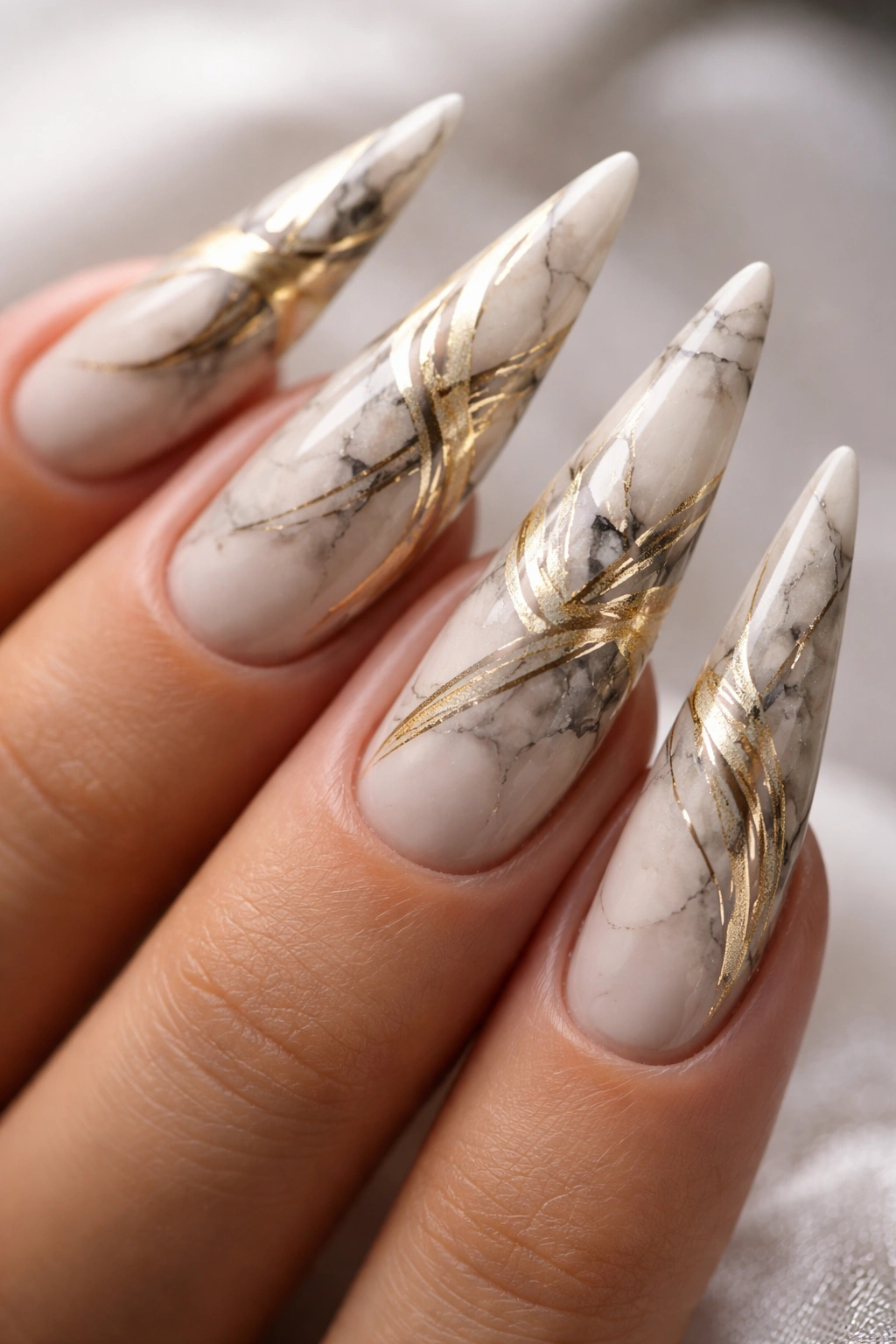 Marble nail design with metallic gold swirls on stiletto nails.