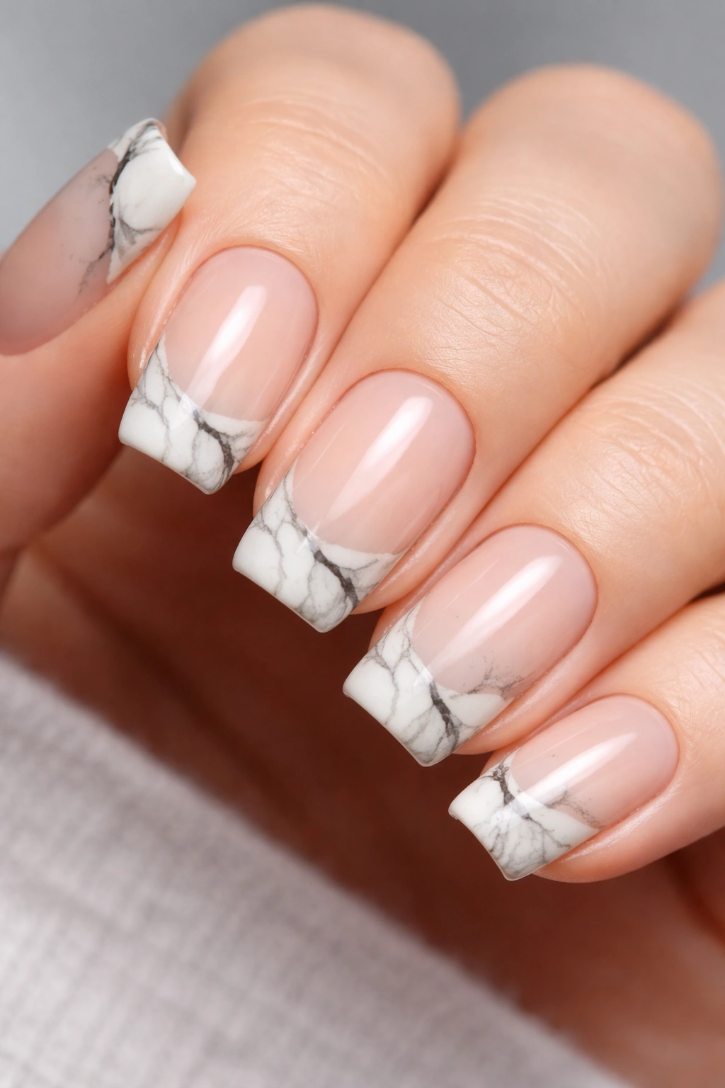 Close-up of short squoval nails with marble tips on nude base featuring organic veins