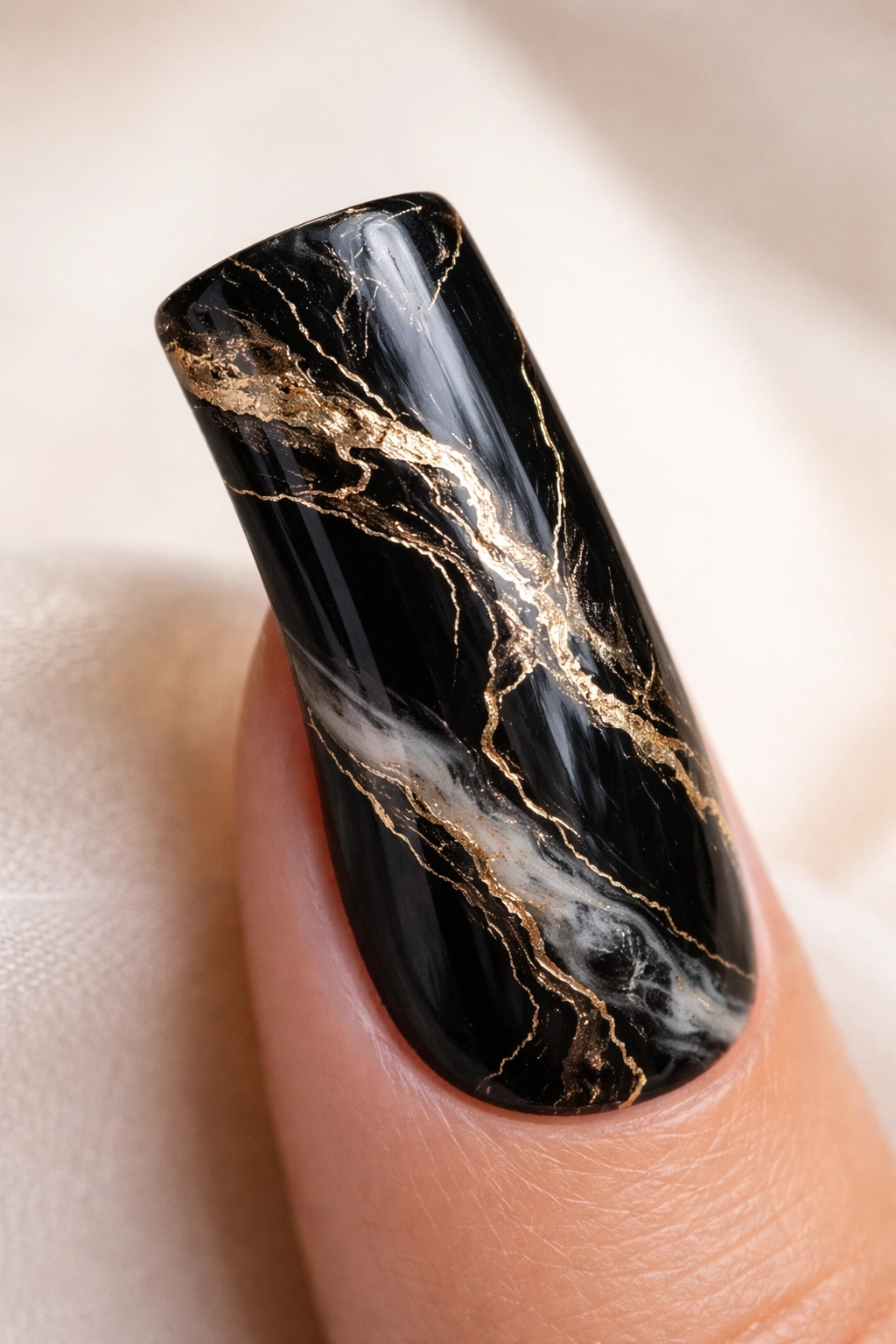 Close-up of a duck nail with black base and gold veined marble pattern