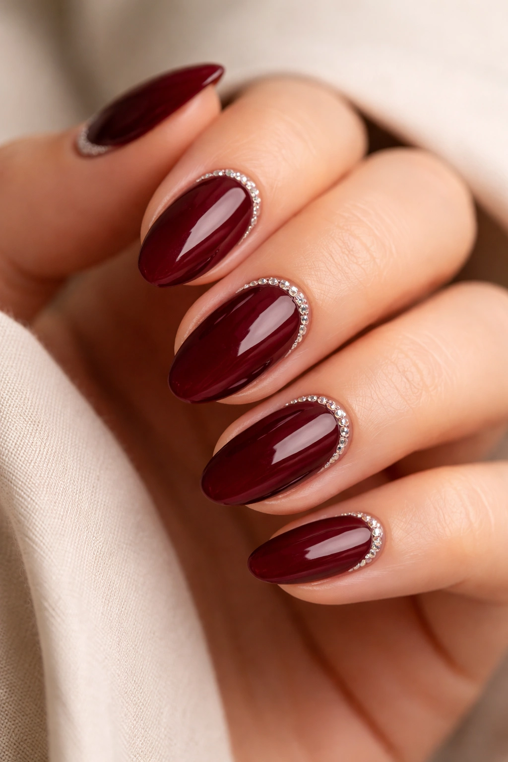 Deep maroon almond nails with tiny crystal outlines along a crescent near the cuticle